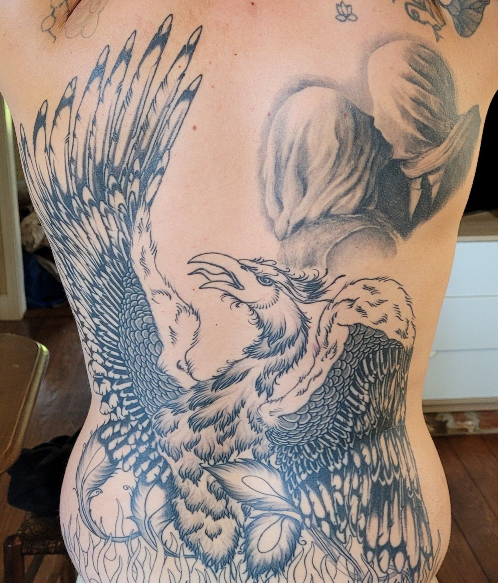 A detailed tattoo of a phoenix covering a person's back