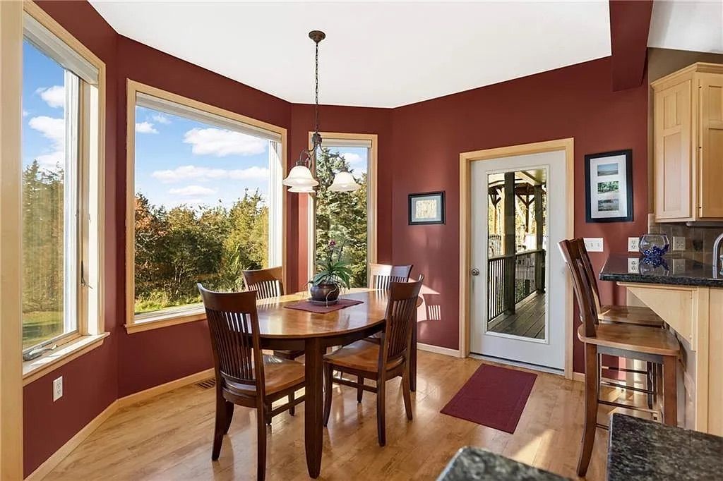 A kitchen with red walls, large windows and a wood table with four chairs.