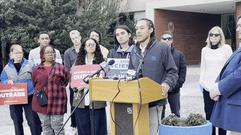 Image shows people talking behind a podium.
