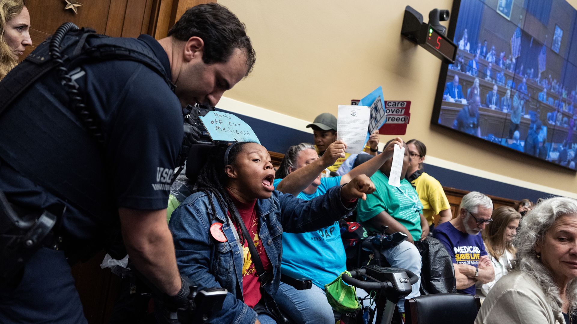 A police officer reaching for a seated woman wearing a denim jacket sitting in a cream-colored room.