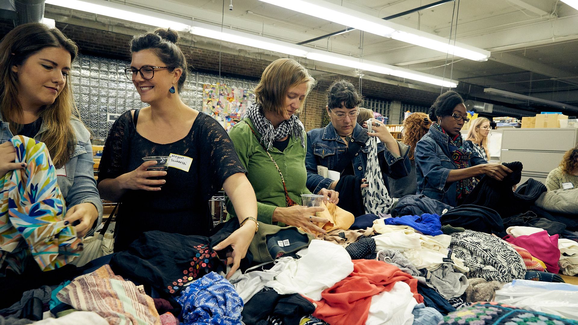 People standing over a table sifting through shirts on the table.