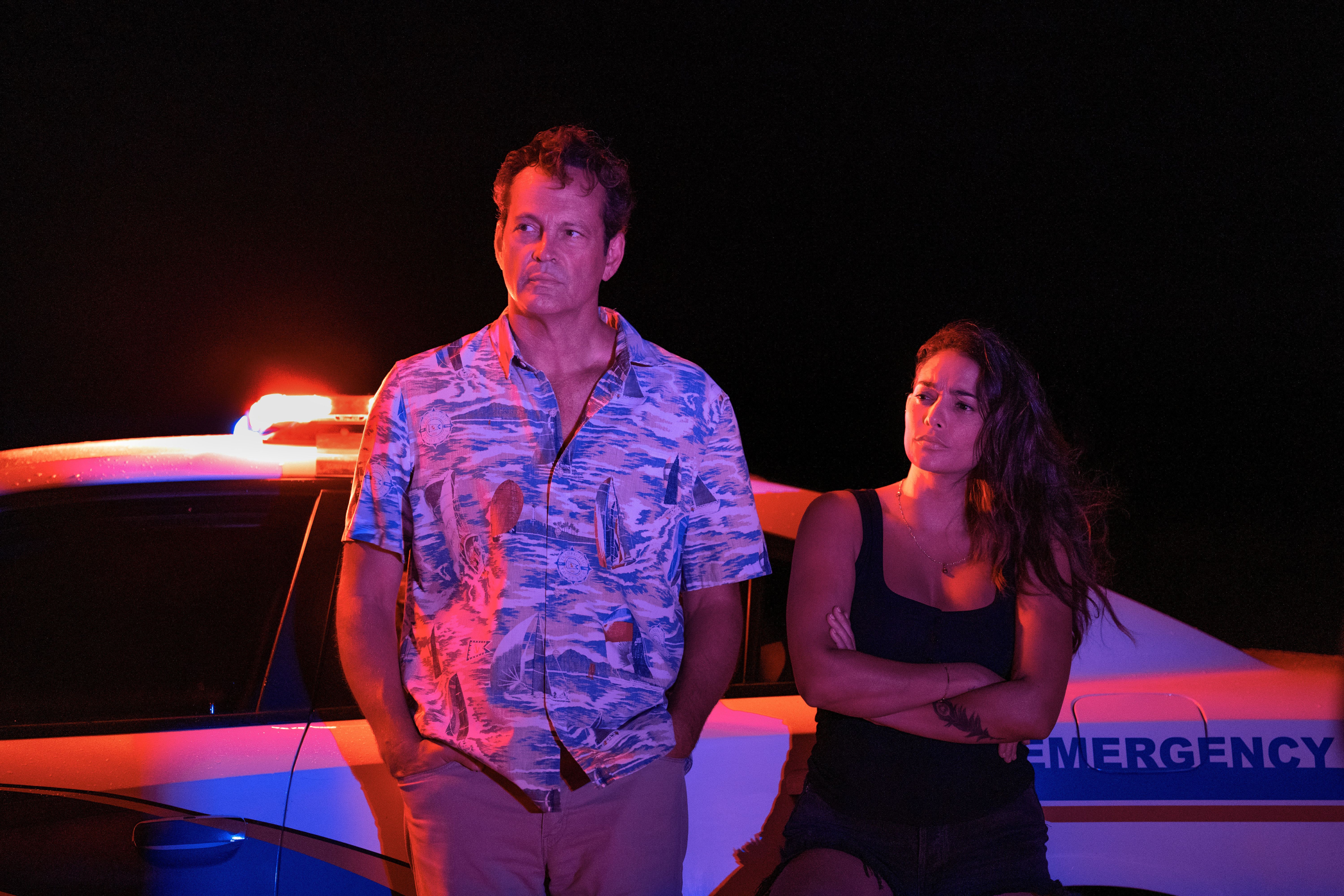 Actors Vince Vaughn and Natalie Martinez stand in front of a police car at night in an image from "Bad Monkey."