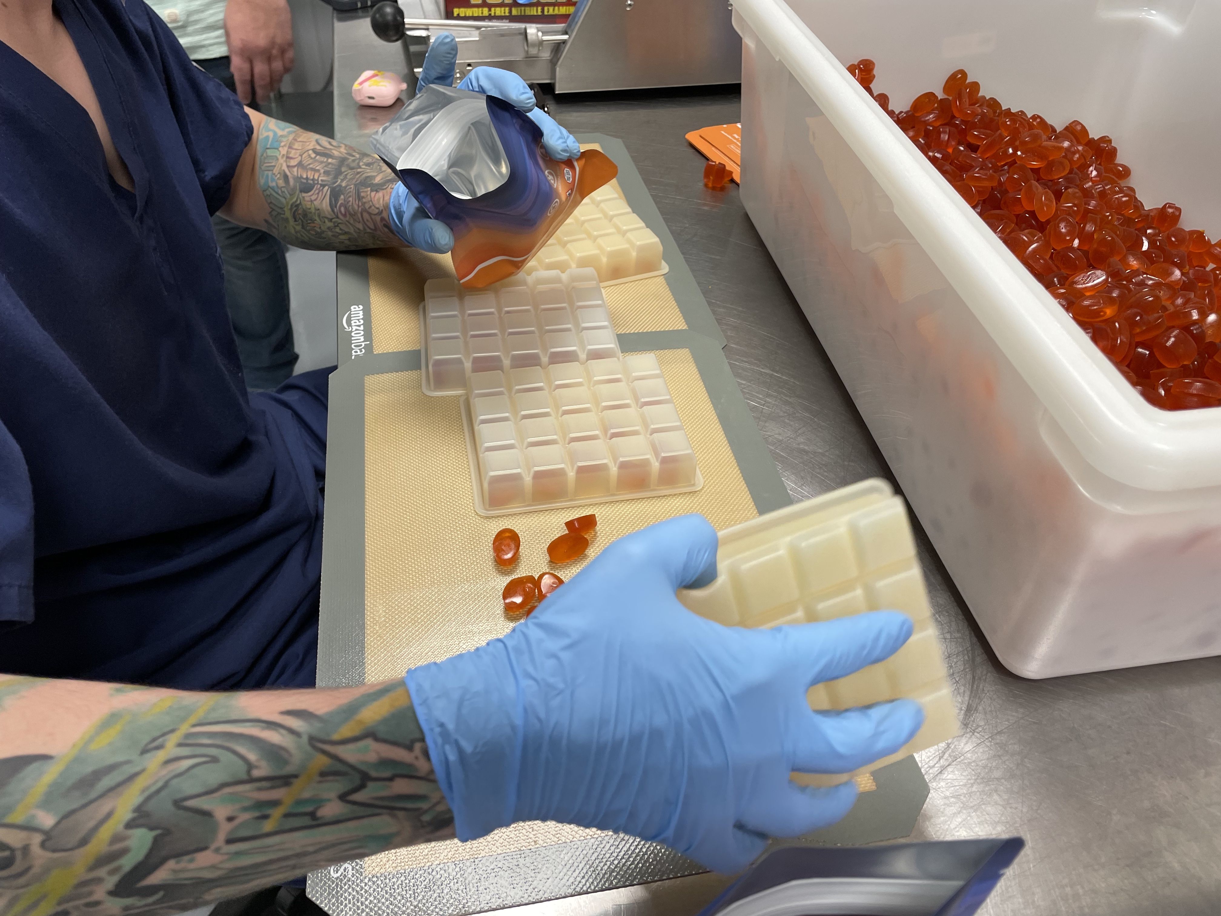 A close up of an employee's hands, with blue gloves, as he counts edible gummies to put them in their packaging.
