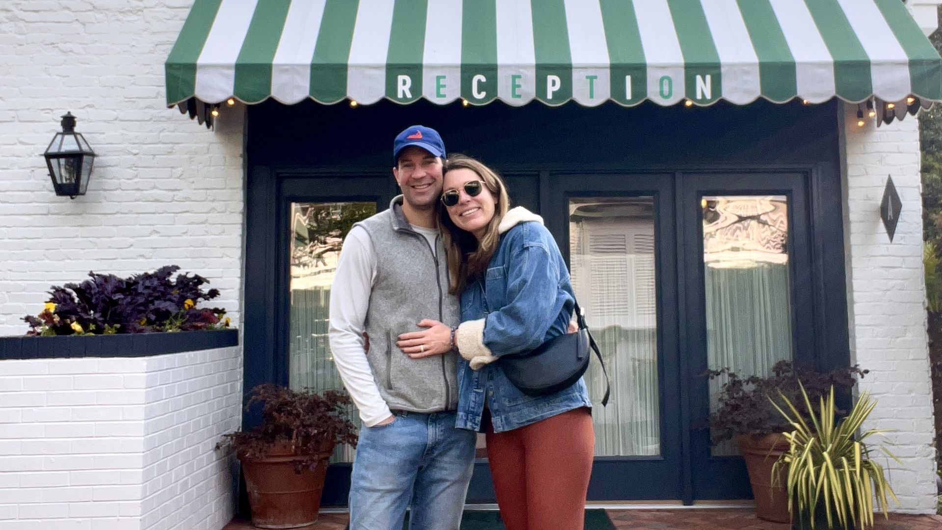 A man and a woman hugging in front of an awning reading "Reception." 