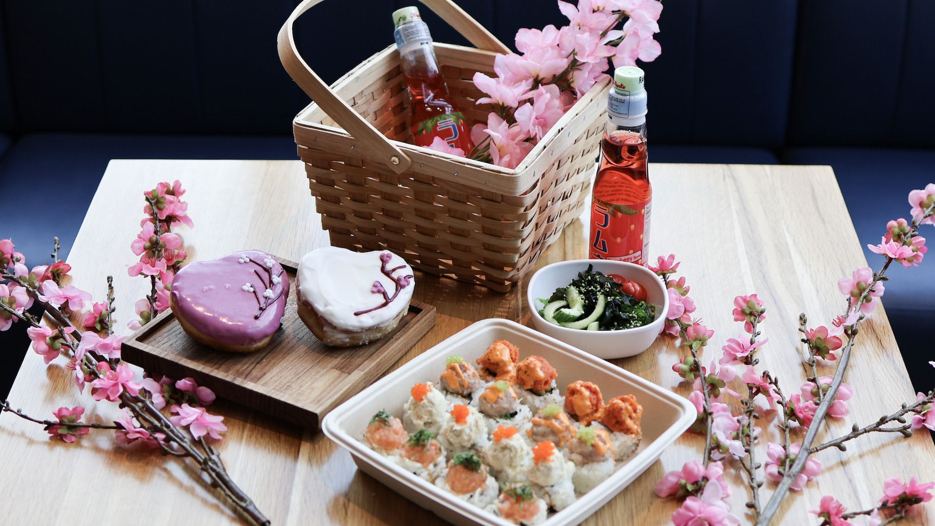 A cherry blossom table with sushi, a picnic basket, doughnuts and blooms