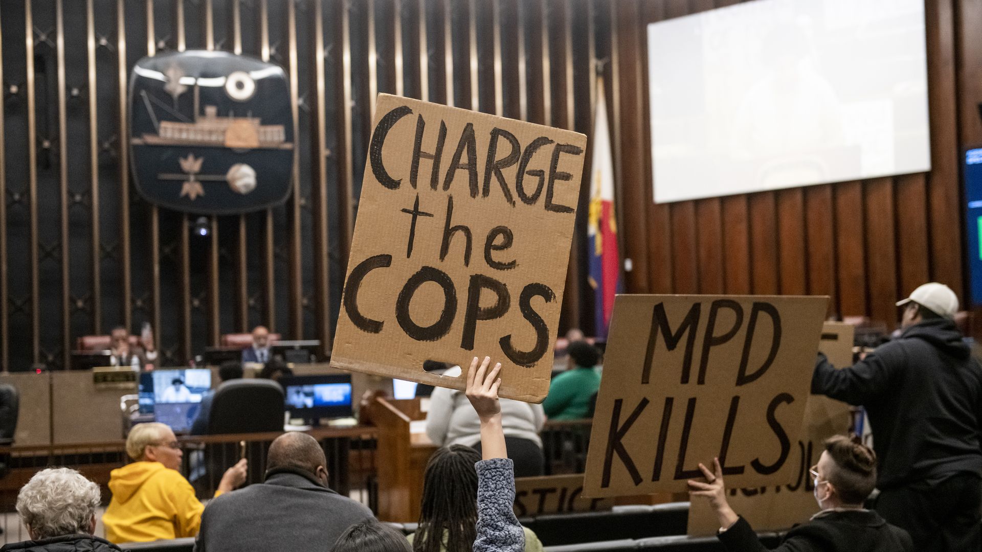 Photo of people holding signs at a Memphis city council meeting, with one marked "Charge the cops" and the other "MPD Kills"