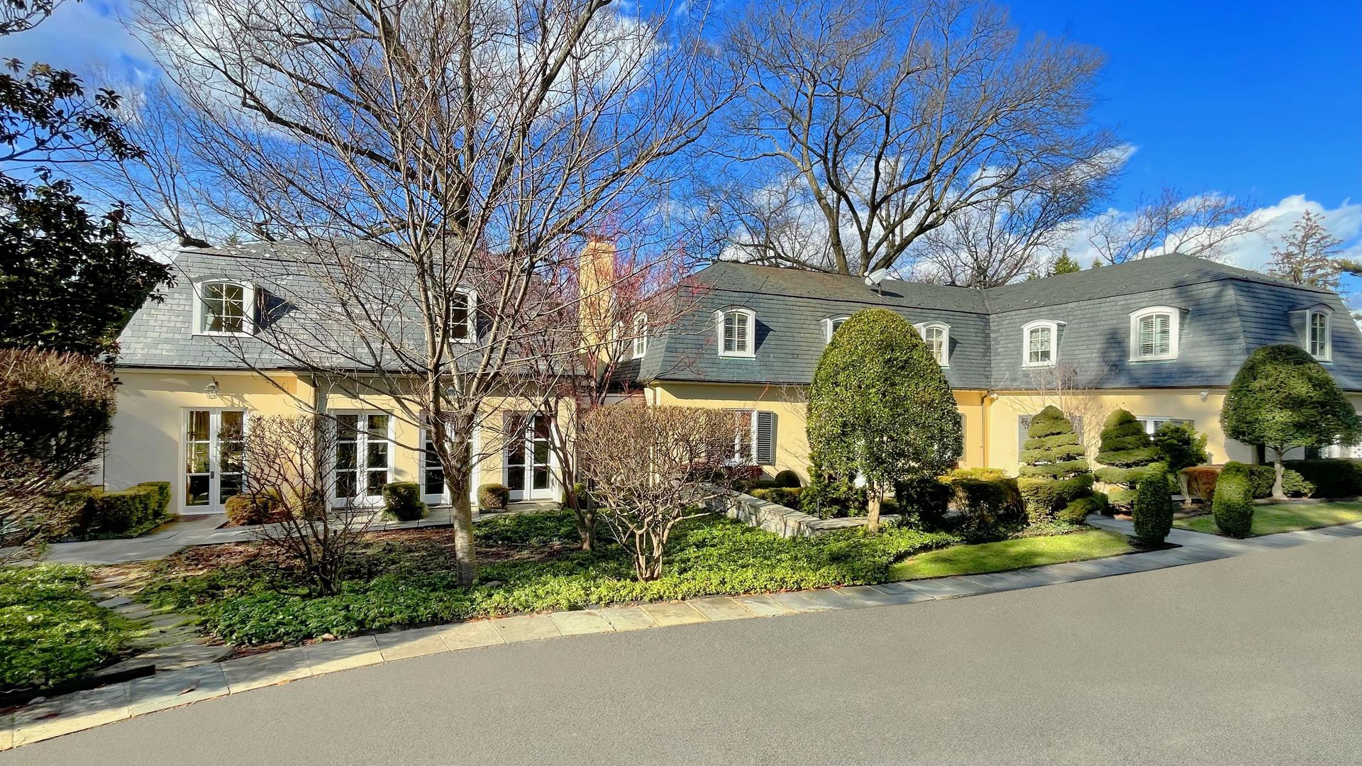 The exterior of a house with a yellow facade, gray roof and trees in the front yard.