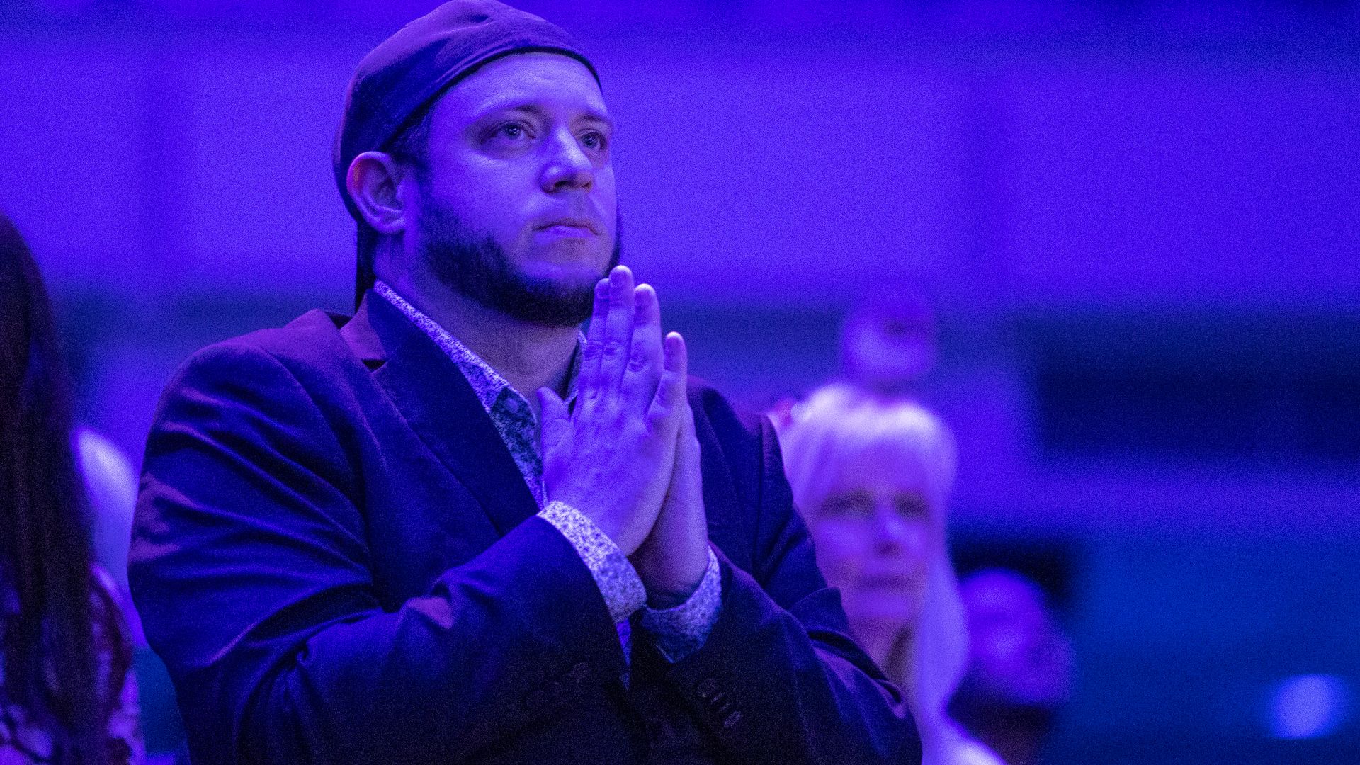A bearded man in a backwards hat and suit, praying