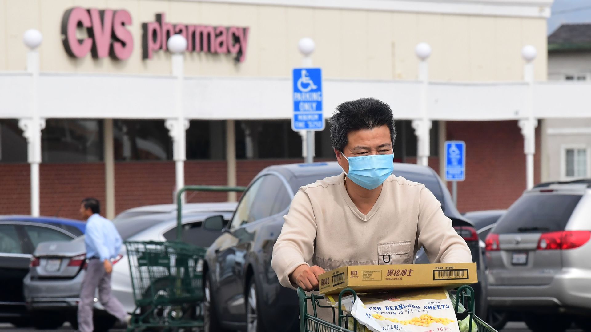 In this image, a man wearing a face mask pushes a shopping cart through a CVS parking lot