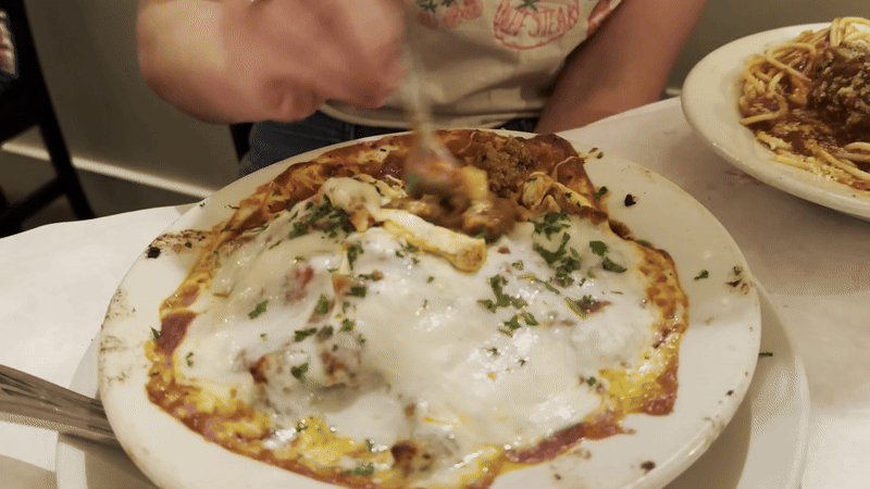 A person dips a fork into a plate of pasta and pulls cheese up as they get ready to take a bite.
