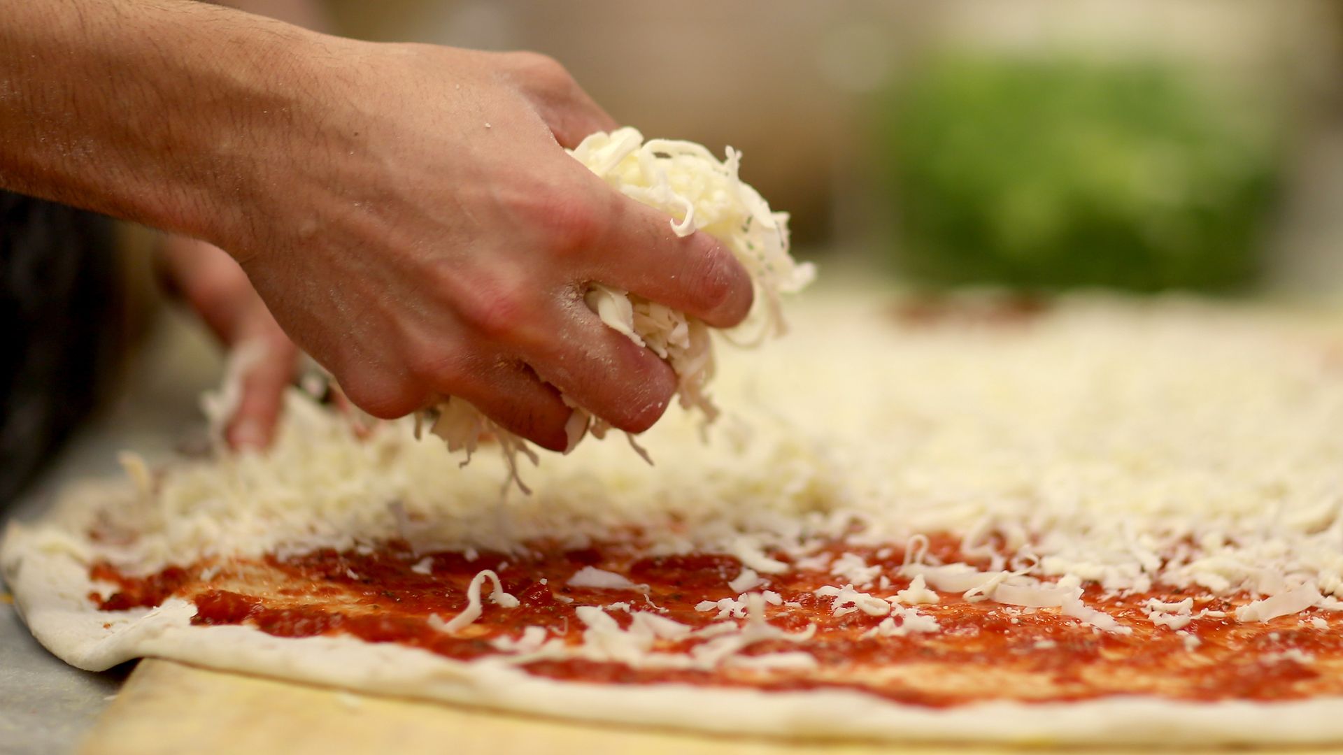 A restaurant employee places cheese on a pizza dough.