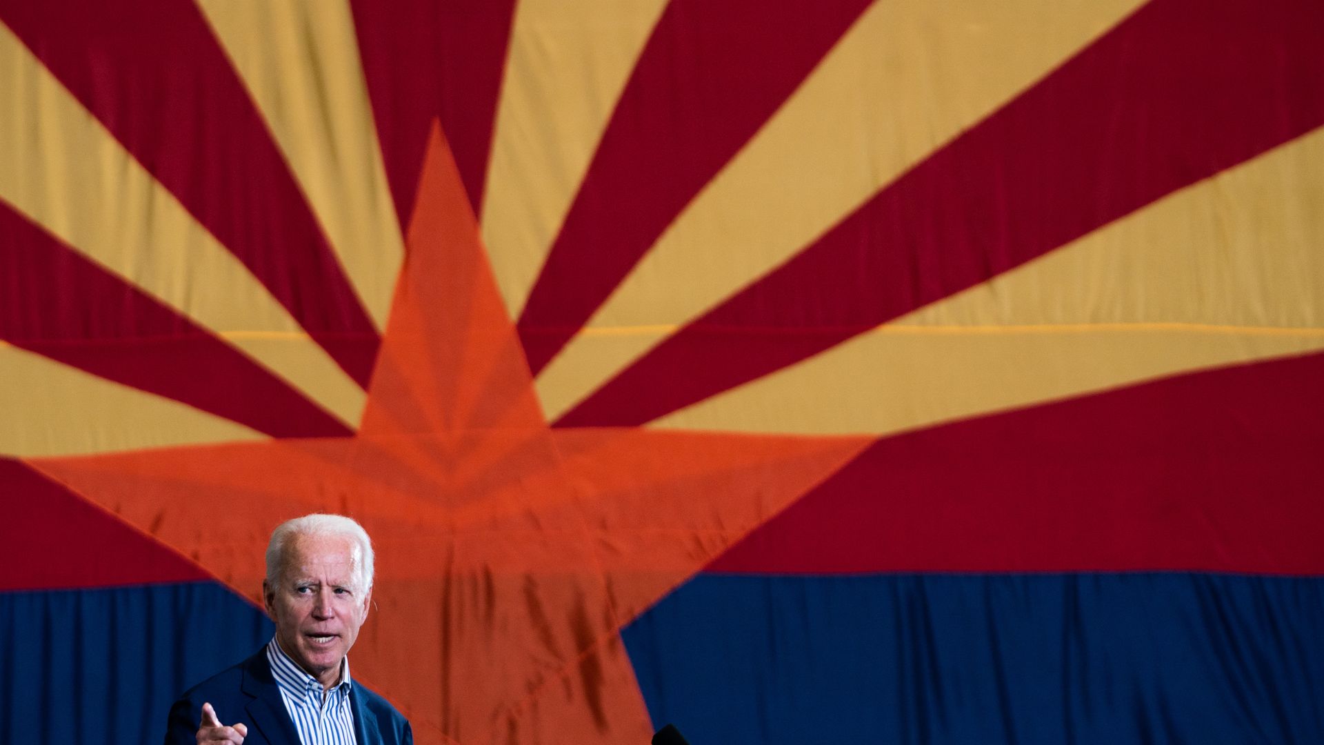 Joe Biden speaks in front of a large Arizona state flag.