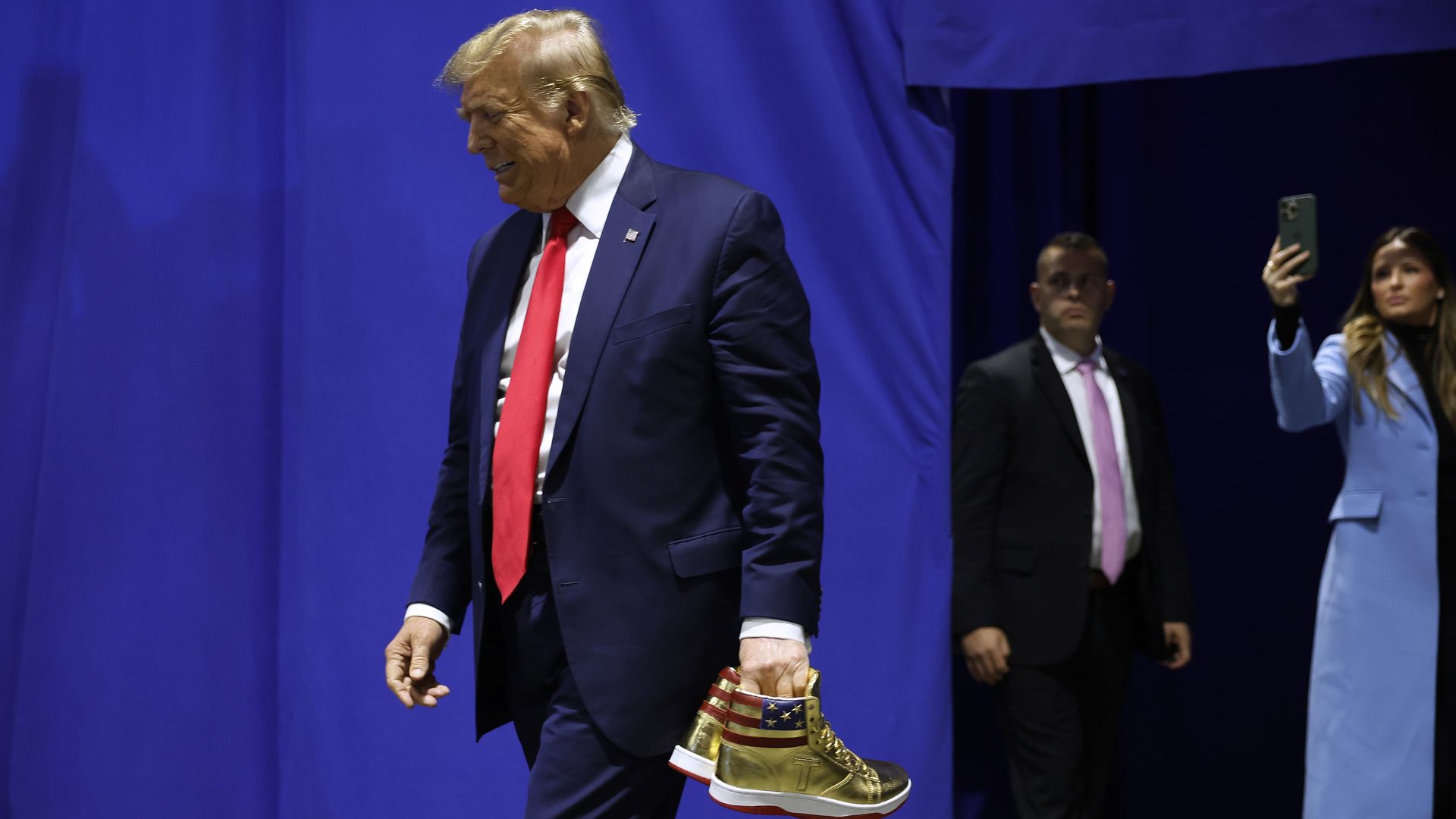 Trump carries a pair of his gold Trump sneakers.