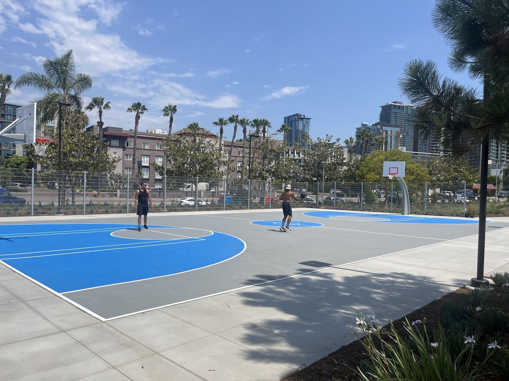 Two men play basketball on an outdoor court at a park.
