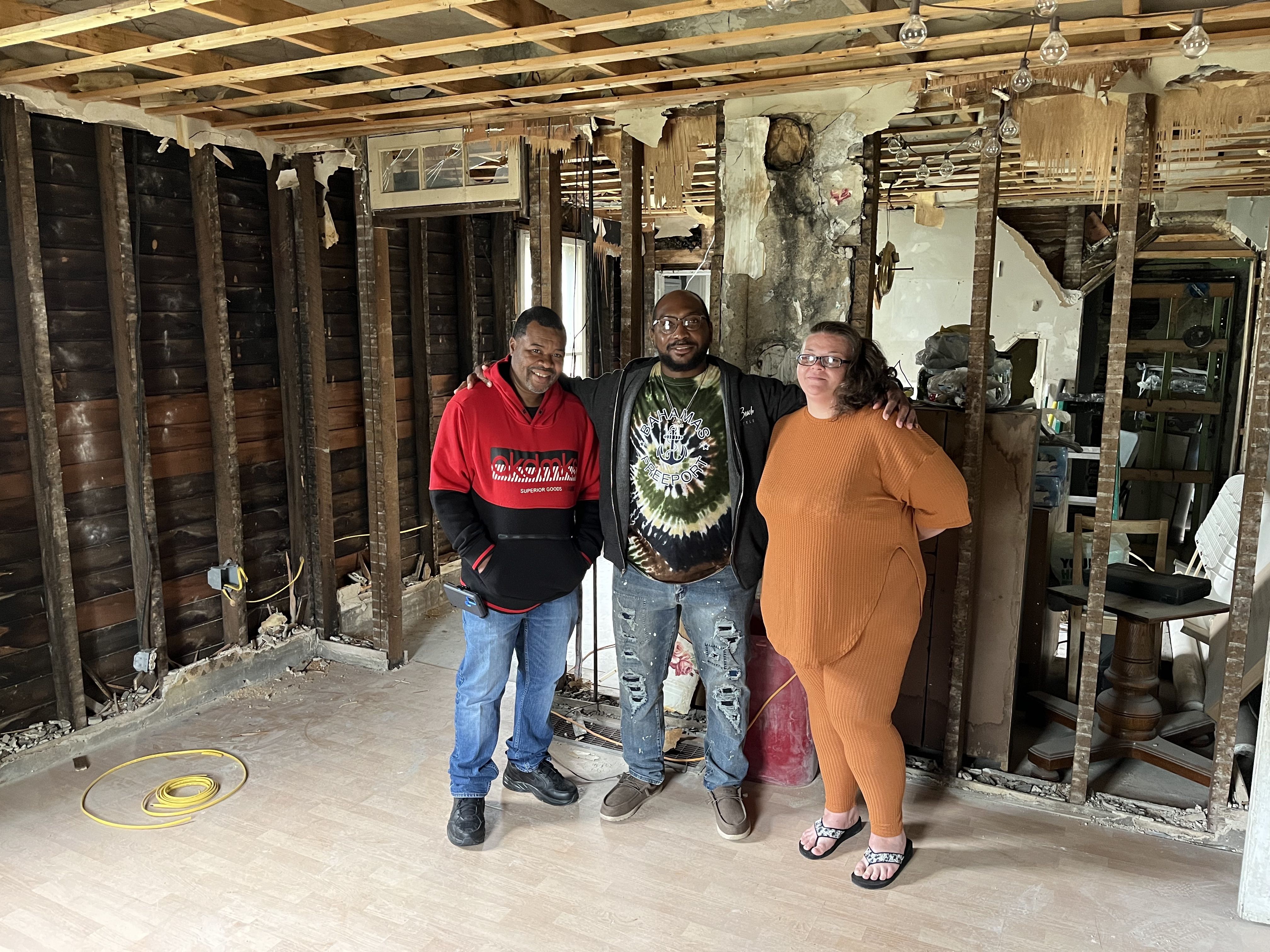 Two men and a woman stand inside a house in the midst of demolition