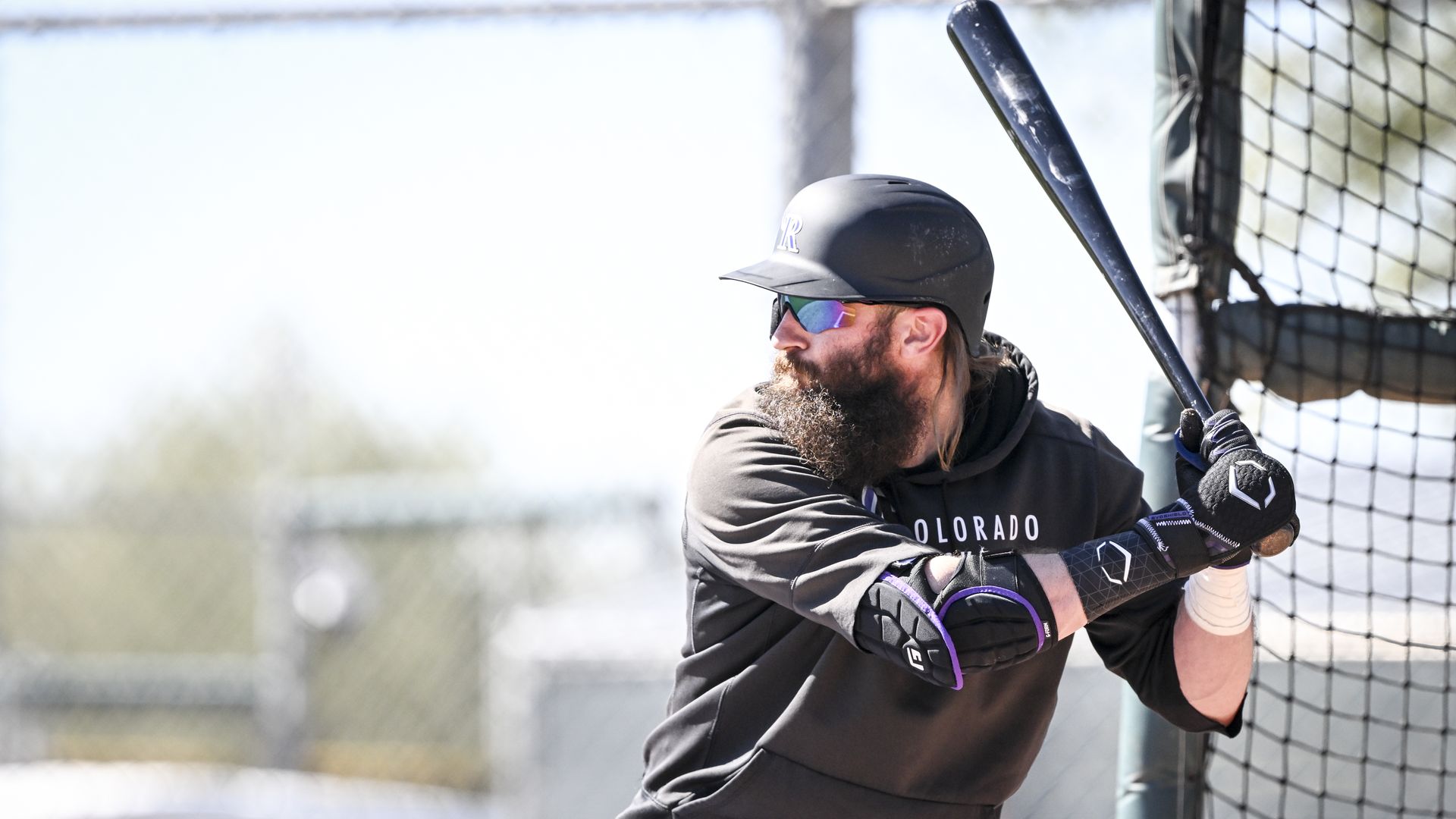 A photo of a Rockies baseball player with a long beard holding up his bat getting ready to swing.