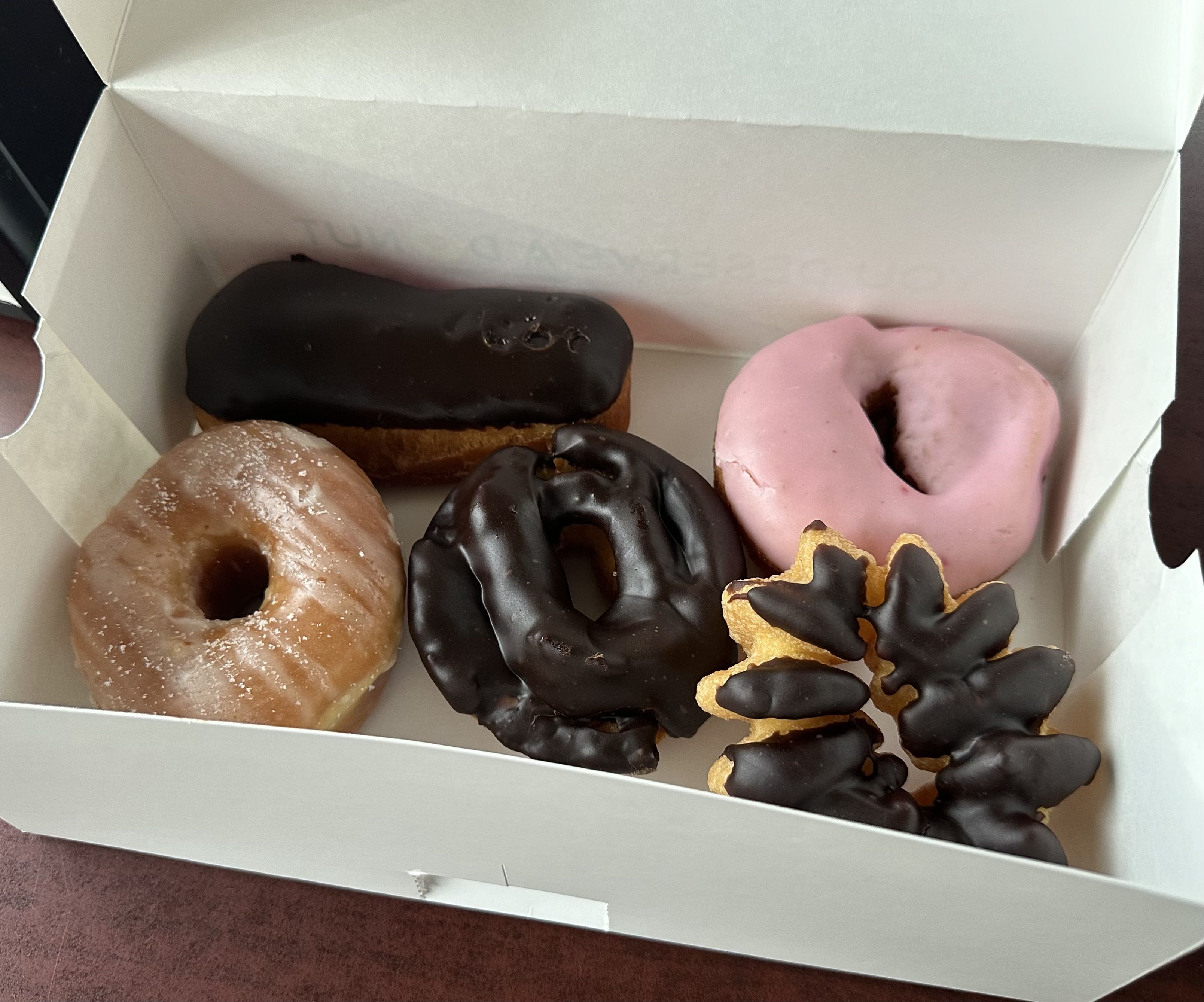 A box of five doughnuts including a pink frosted doughnut, three chocolate frosted doughnuts and a glazed.
