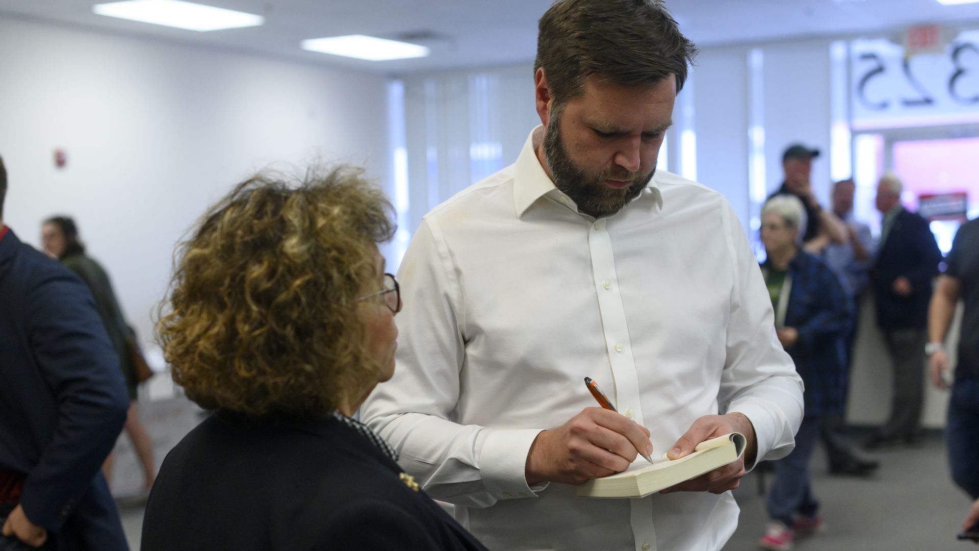 J.D. Vance signs a copy of his book while a lady to his left looks on.