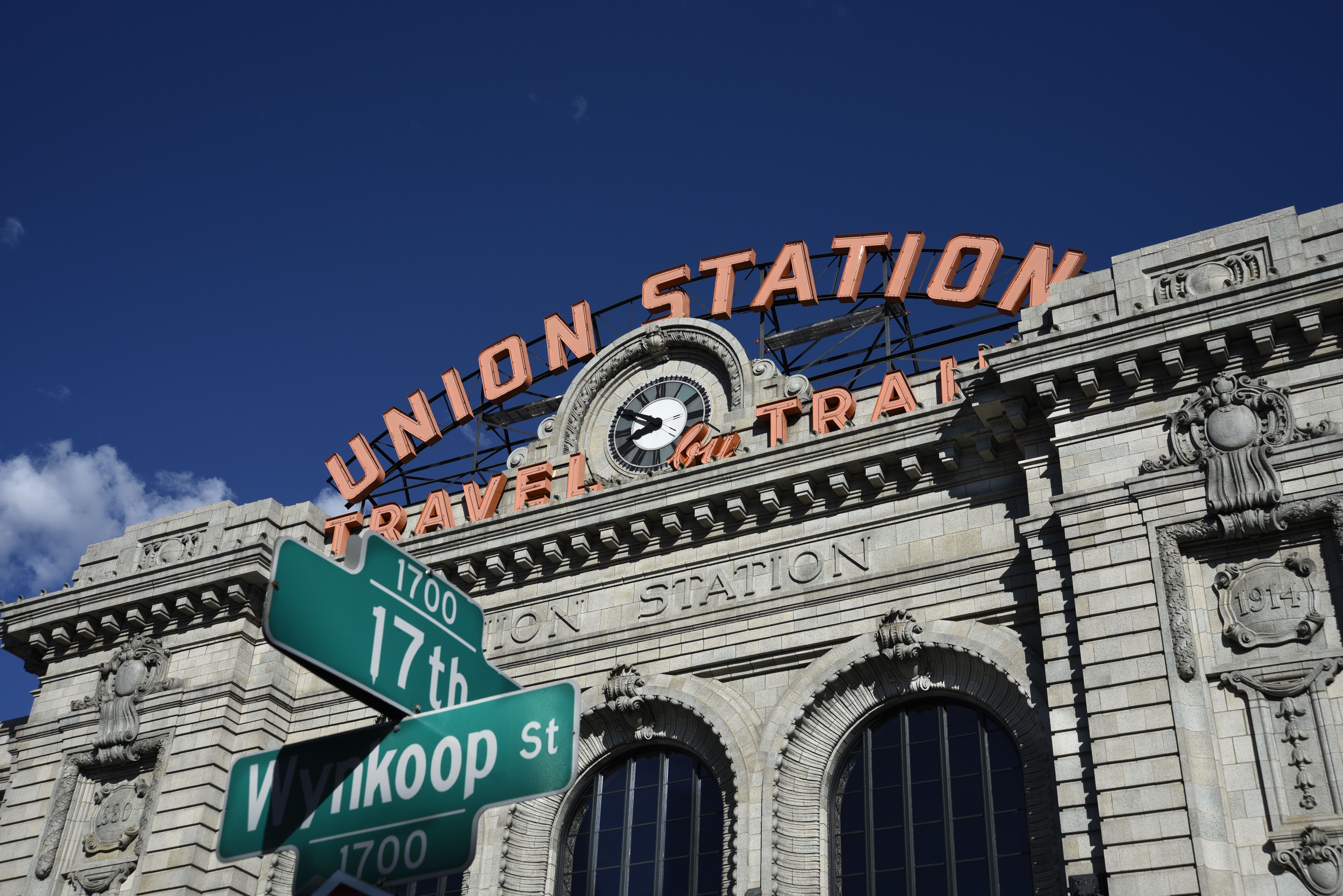 A large, gray structure with the words UNION STATION in orange across its roof. A circular clock is placed under the words, while a street sign with 17th and WYNKOOP ST are in the foreground.