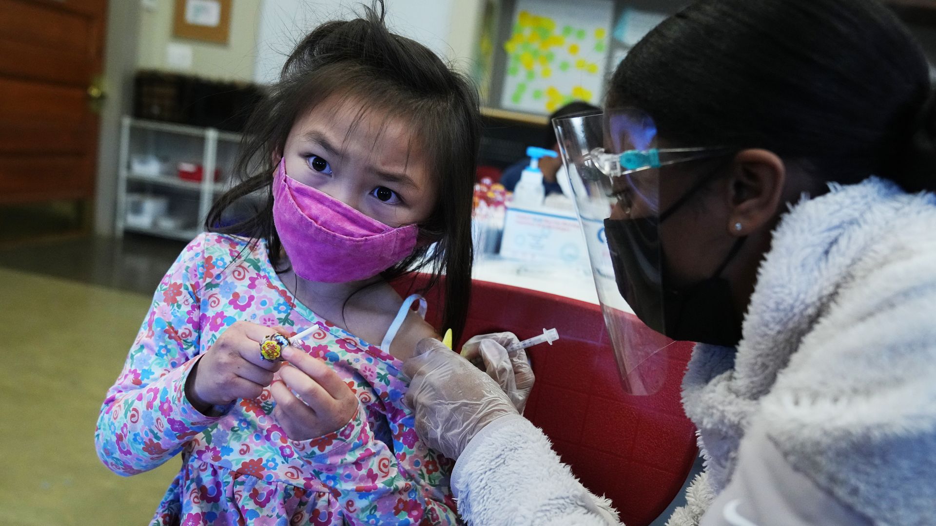 A young girl in a pink mask is vaccinated.
