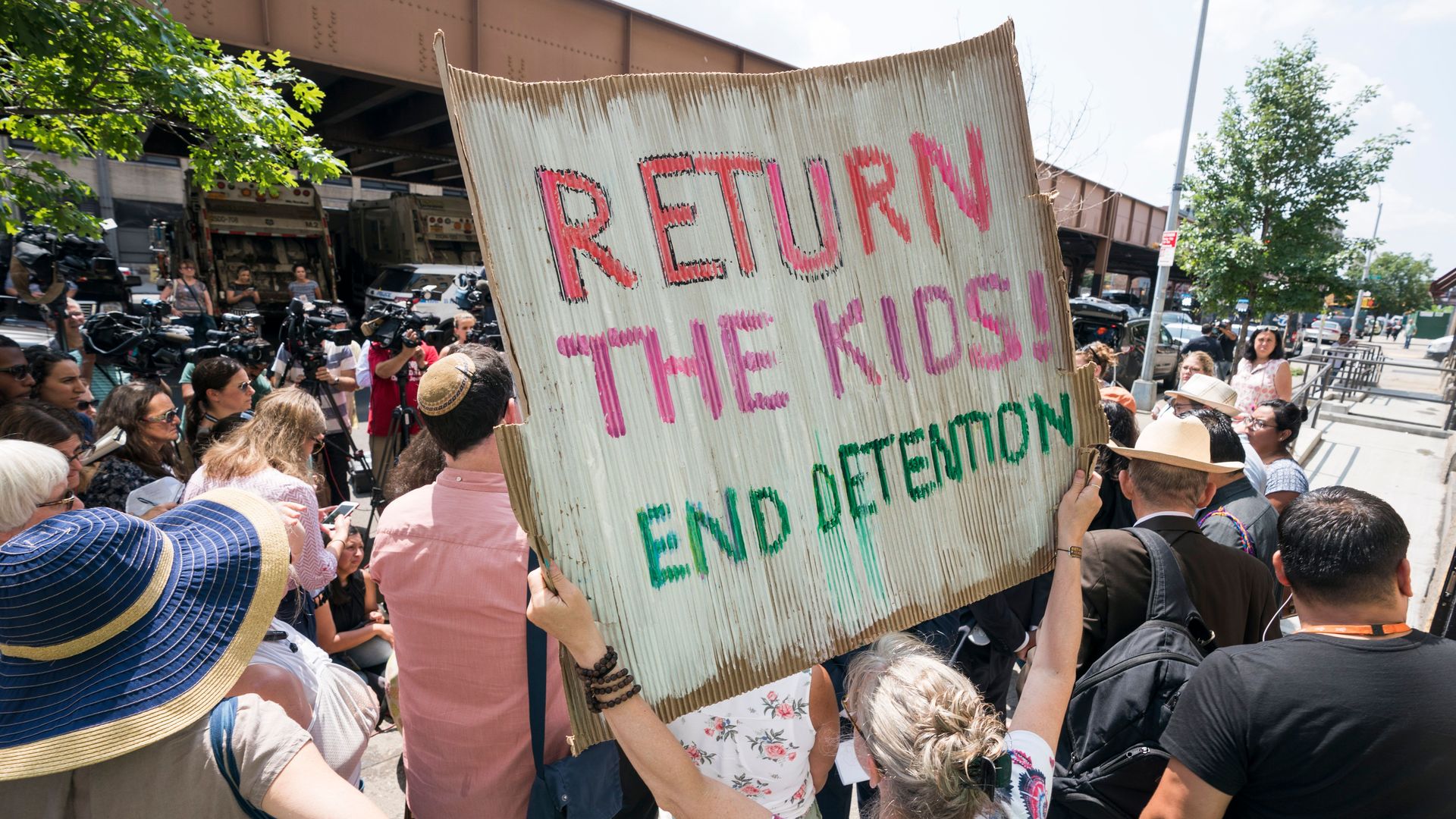 A protestor holding a sign that says "return the kids, end detention"