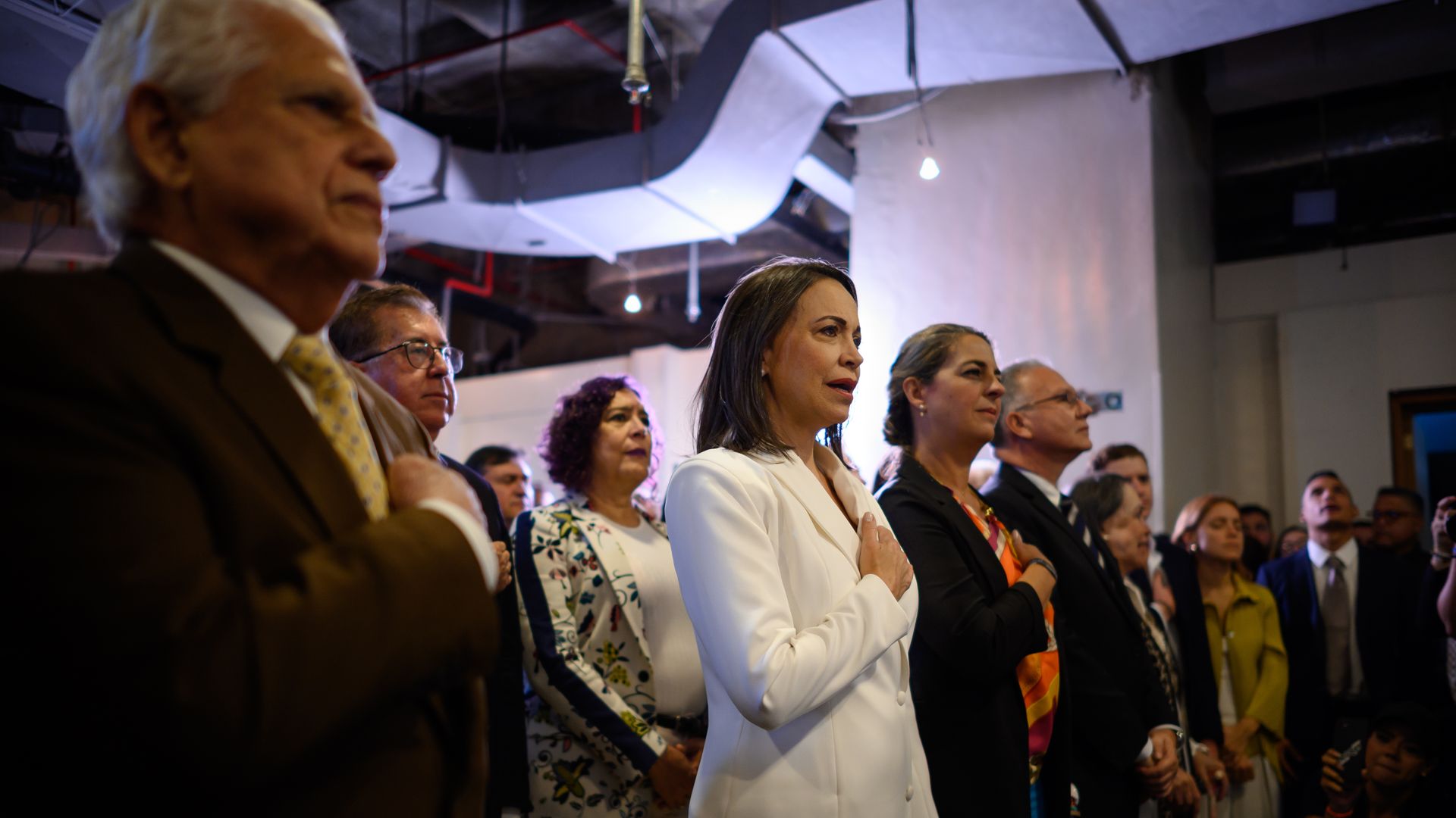 Venezuelan opposition leader Maria Corina Machado stands with her hand to her chest next to several people