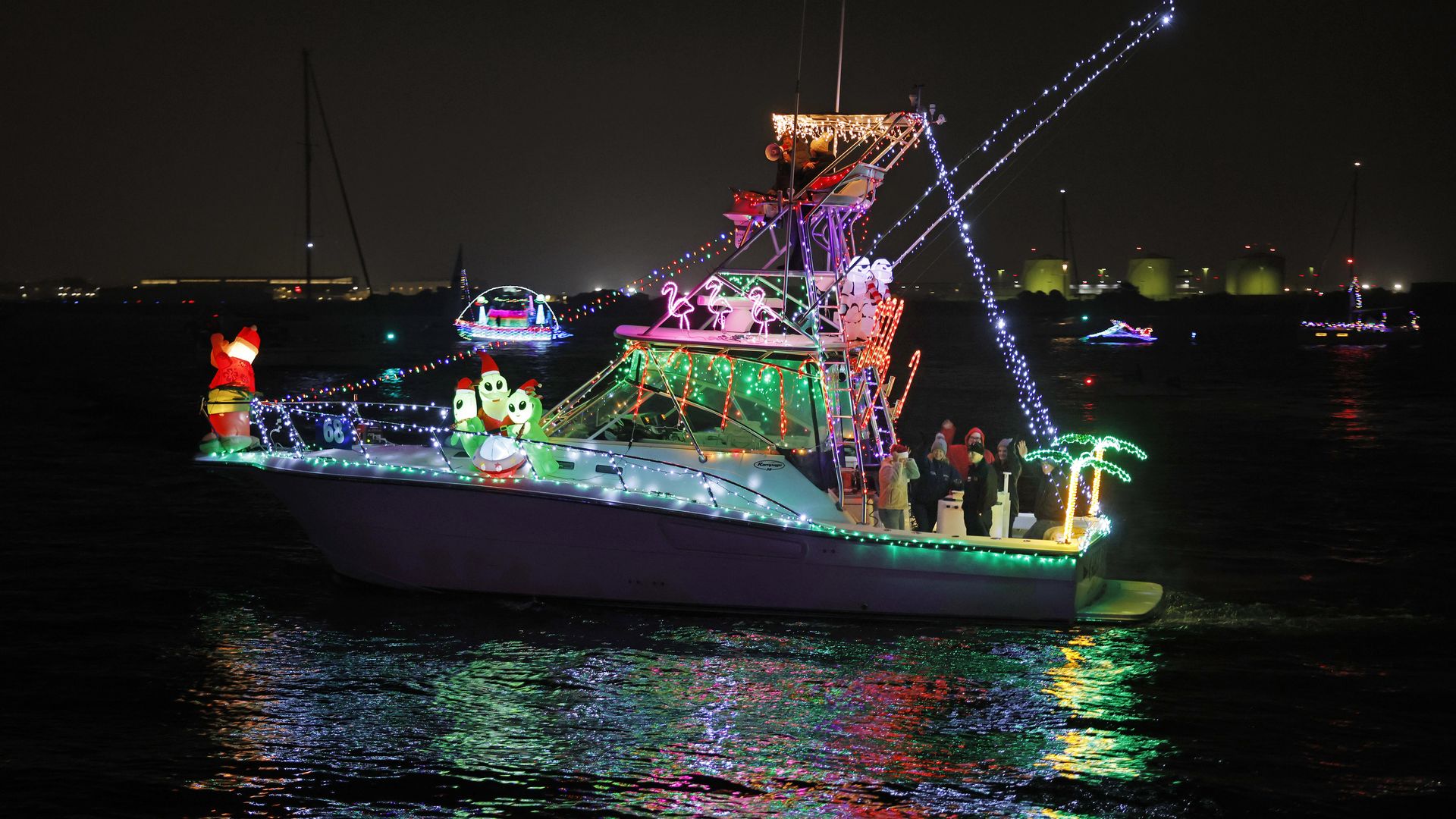 A decorated boat covered with colorful Christmas lights and holiday-themed inflatables passes on the San Diego Bay during a parade at night.