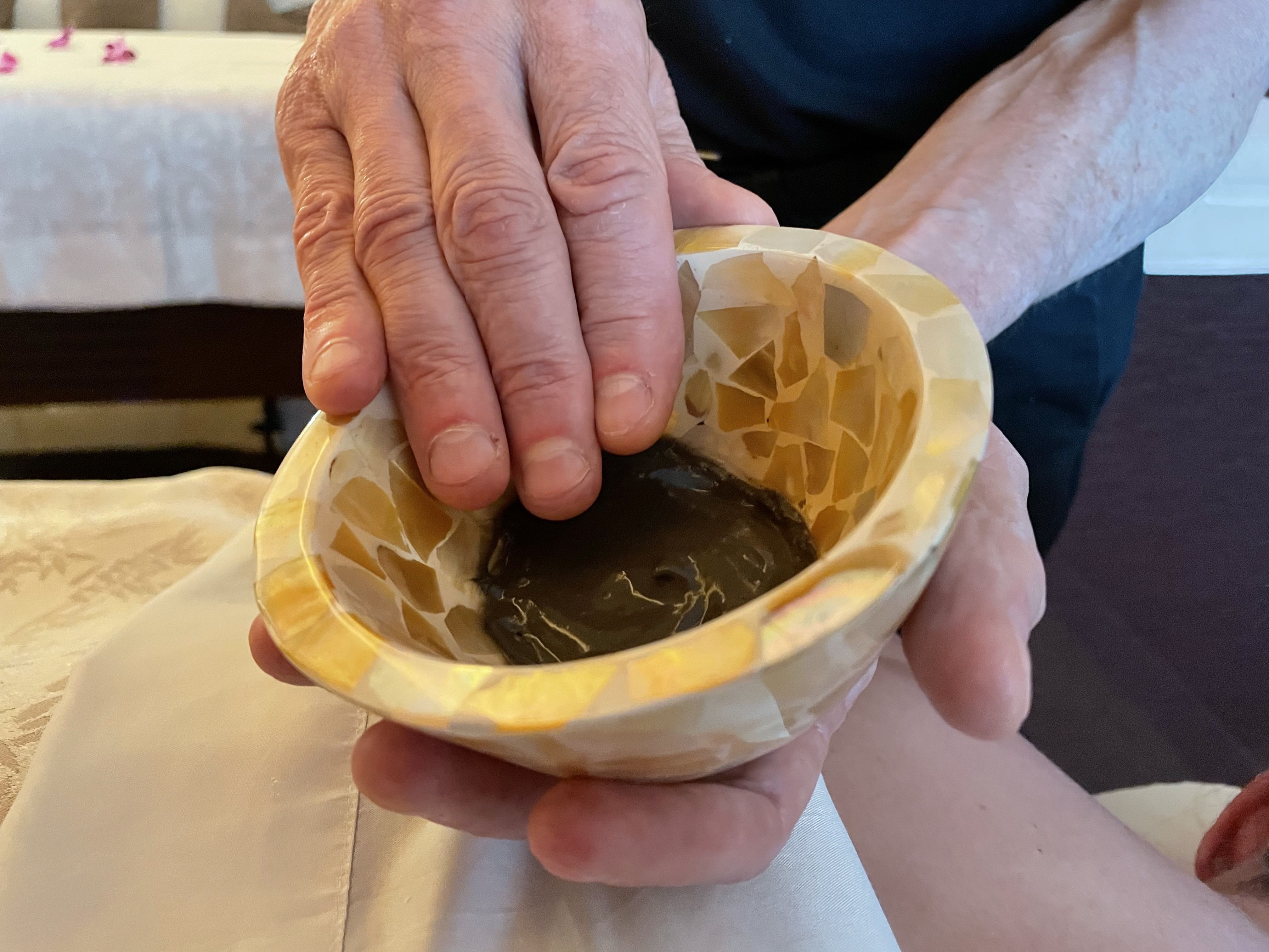 A massage therapist holds a small bowl with a mud product he is about to apply on a client's back.