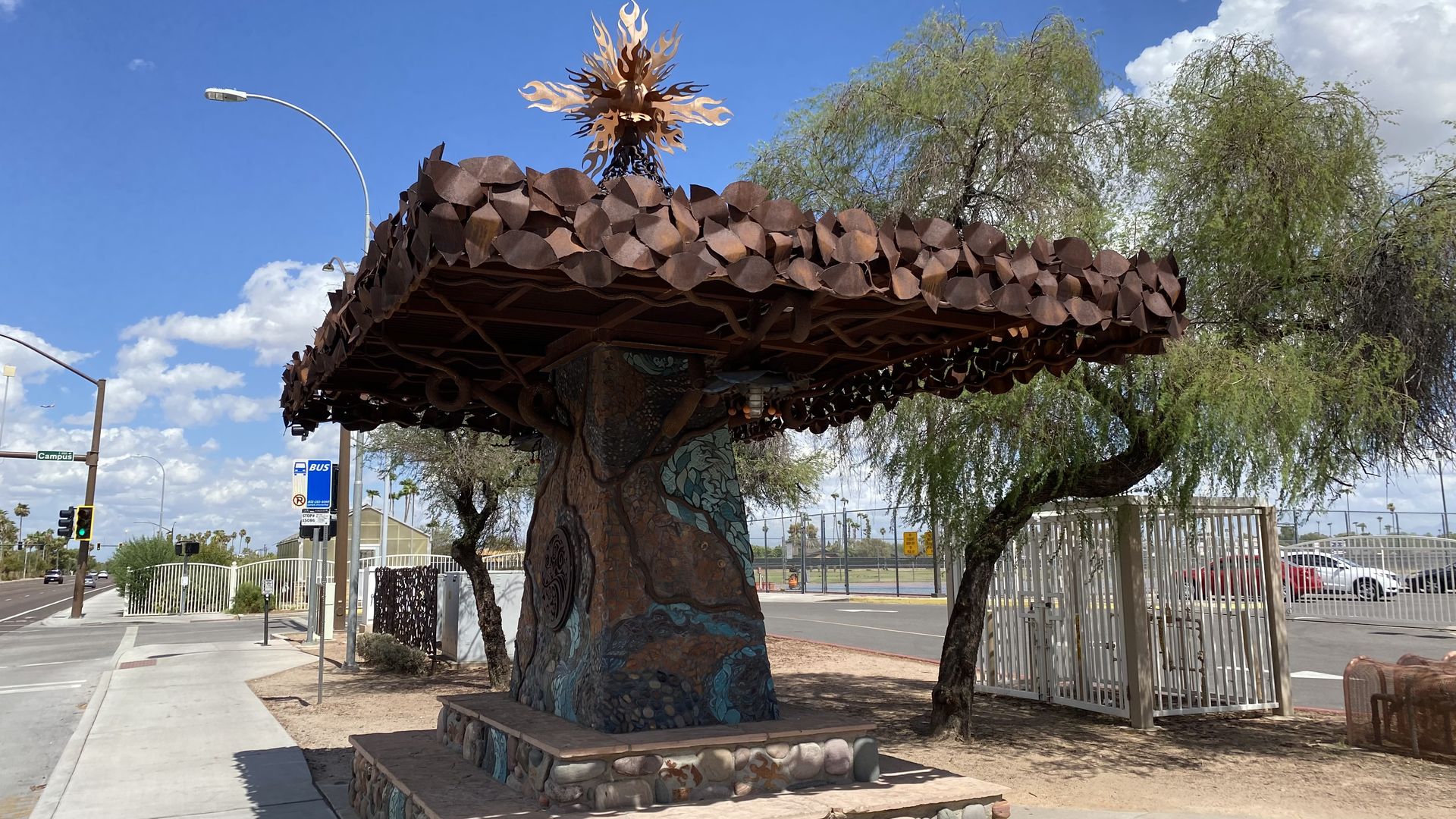 A bronze colored metal tree-like sculpture with turquoise designs on the squared trunk and a square shaped canopy.