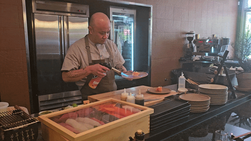 A gif of a chef using a small torch on a sushi plate