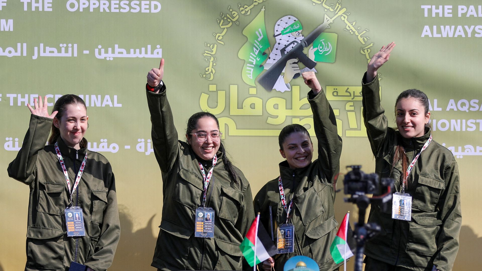 Four women wave in matching dark green jackets with logo panel behind them