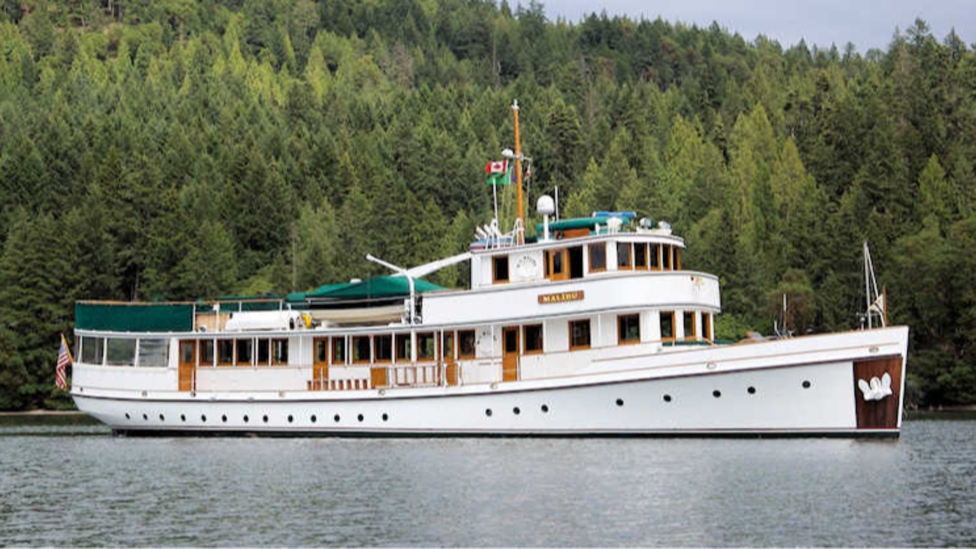 A 100-year-old wooden yacht with white paint and natural wood and green trim.