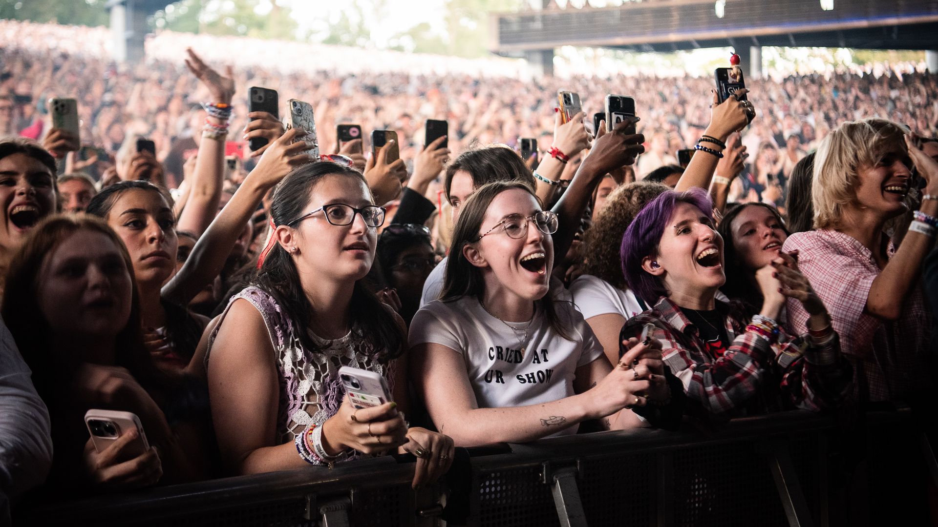 A photo shows people standing in a crowd in front of a stage listening to a concert.
