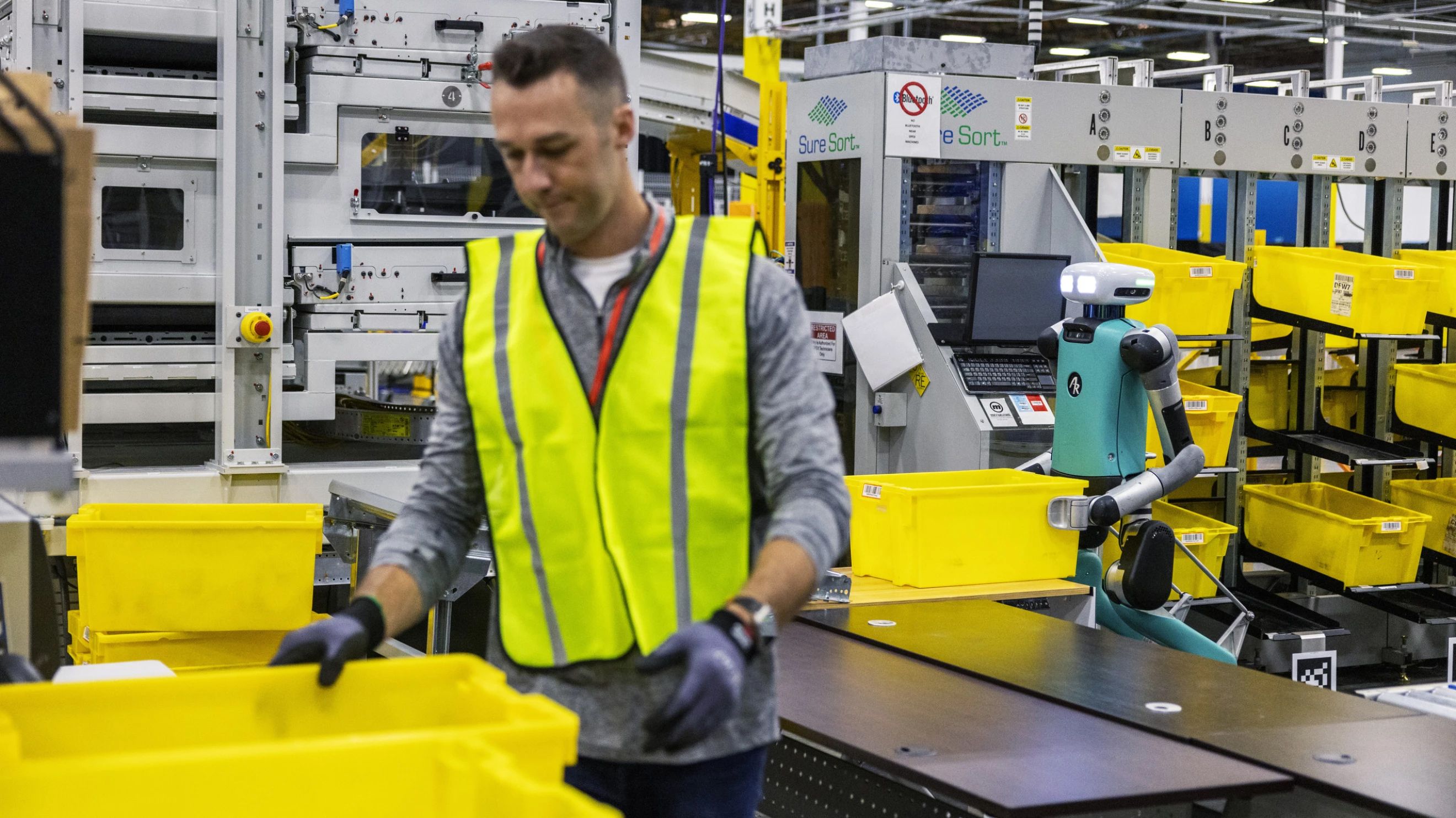 A human warehouse worker toils alongside a robot one.