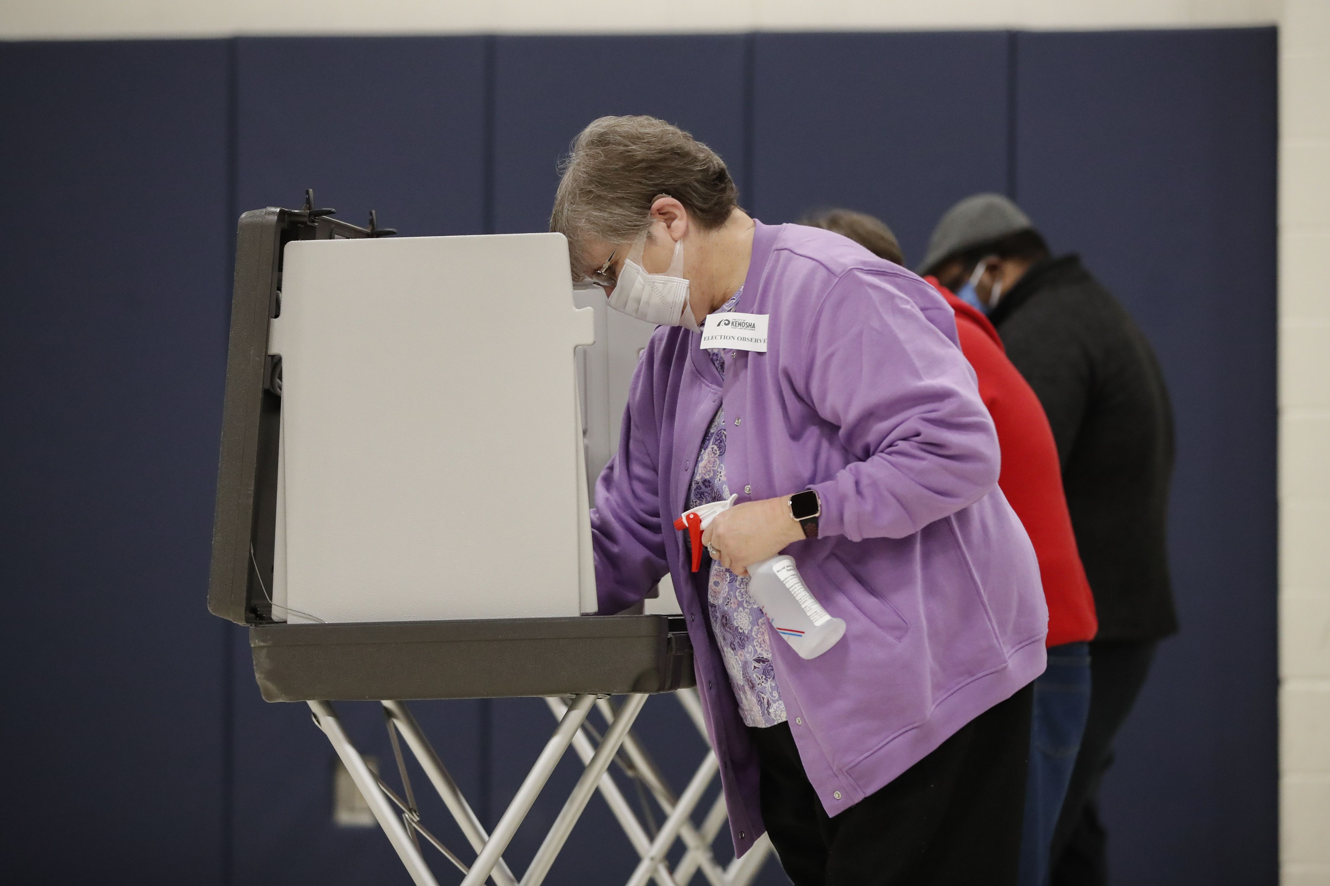 In this image, a woman cleans and wipes down a voting booth