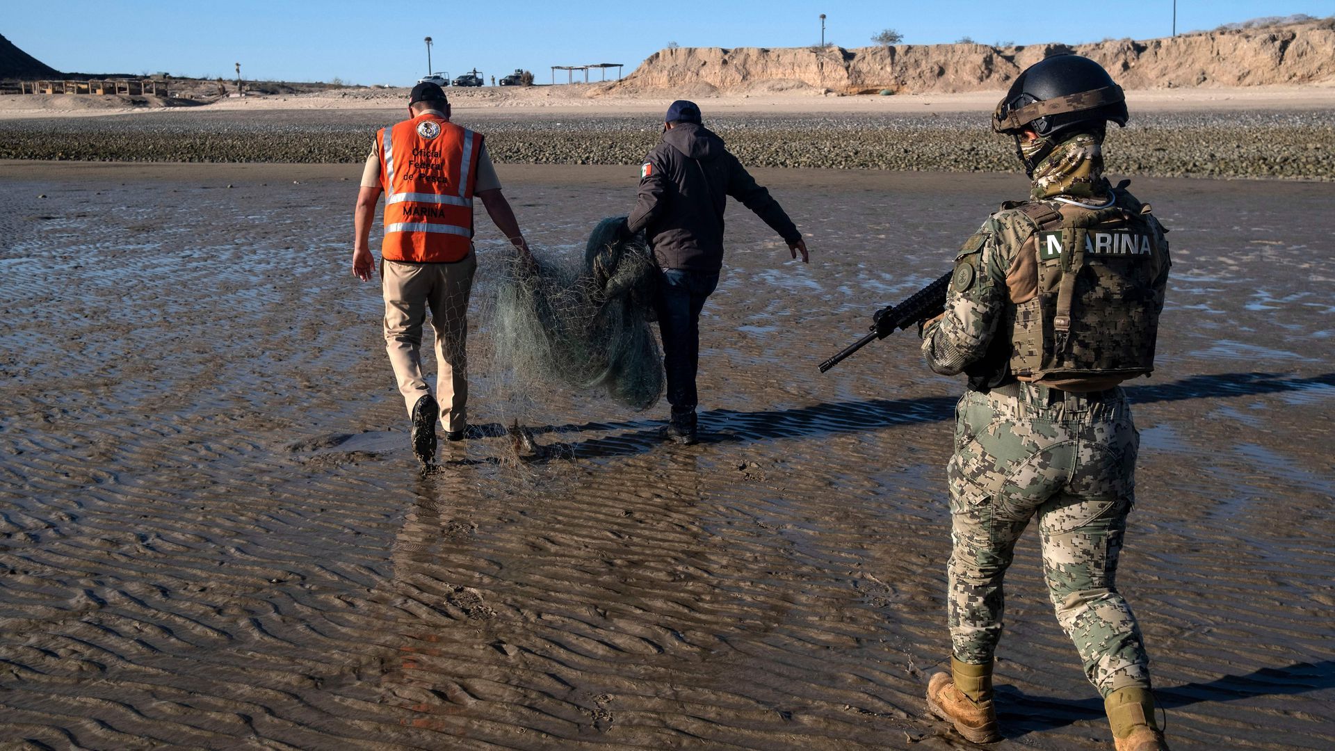 An armed Mexican Navy officer walks behind two people carrying an illegal fishing net in the Sea of Cortez in Mexico