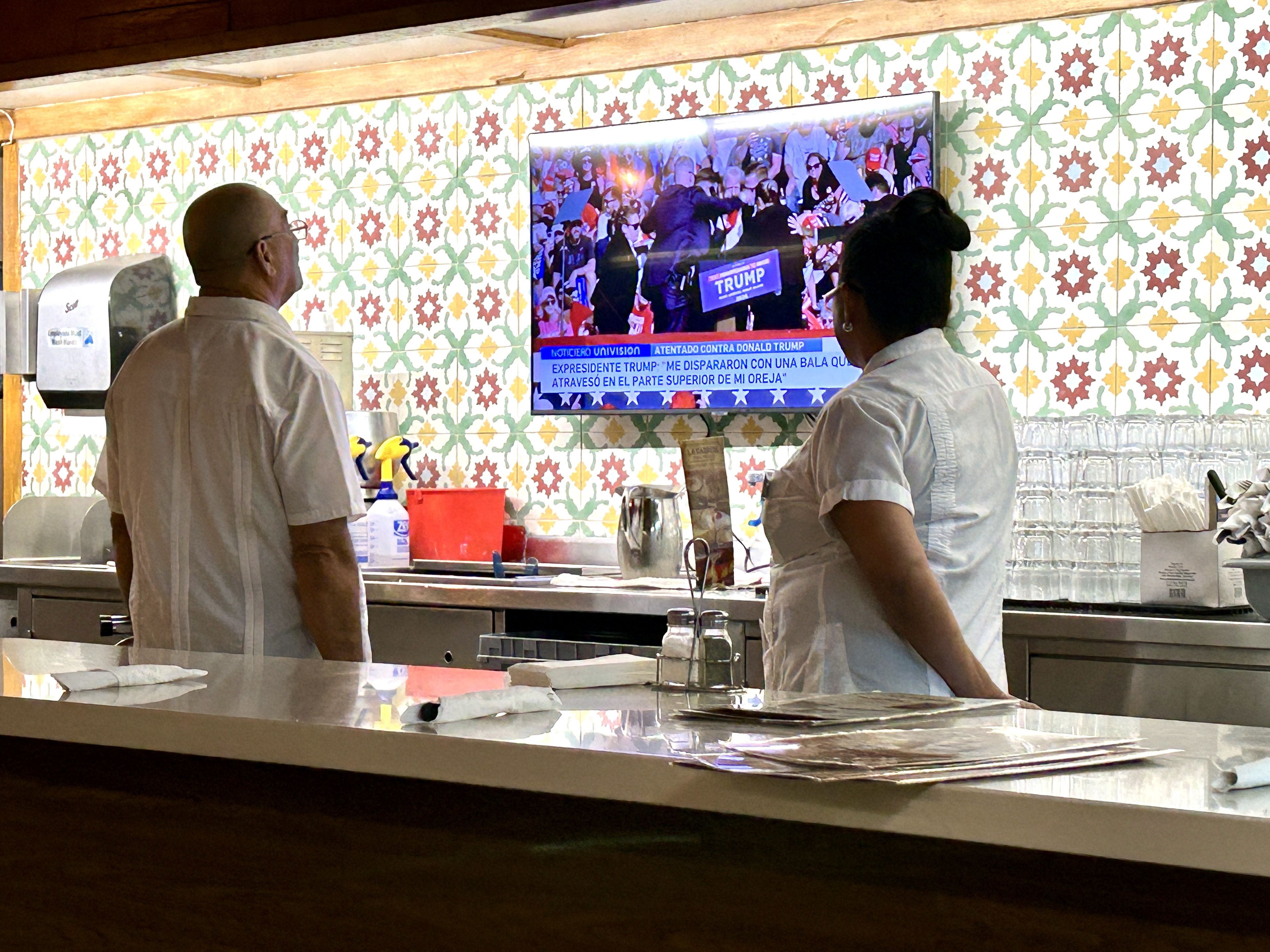 Two employees at a restuarant watch a news report on the rally where former President Trump was shot. 