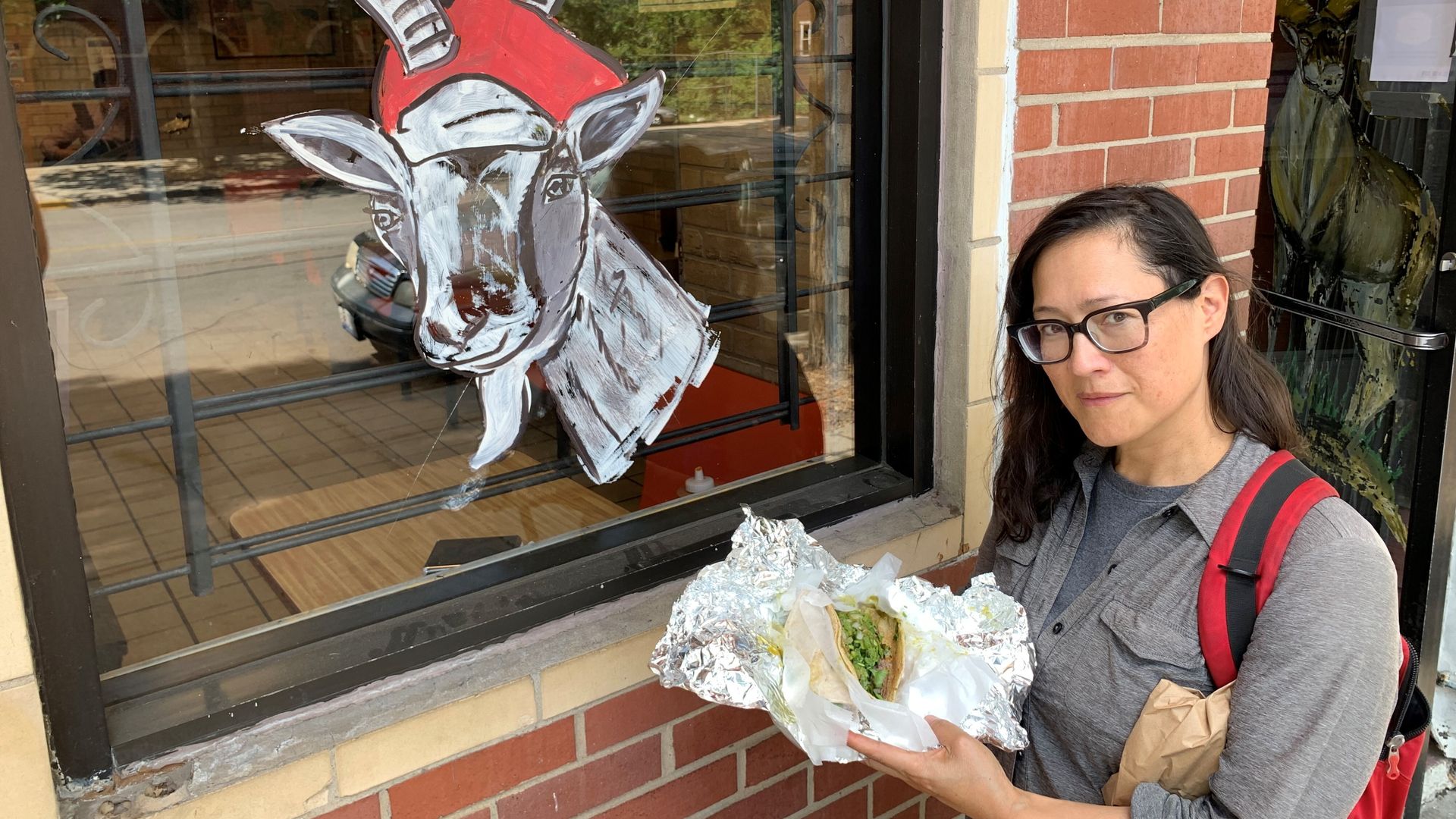 Monica stands in front of a painted goat while eating a taco. 