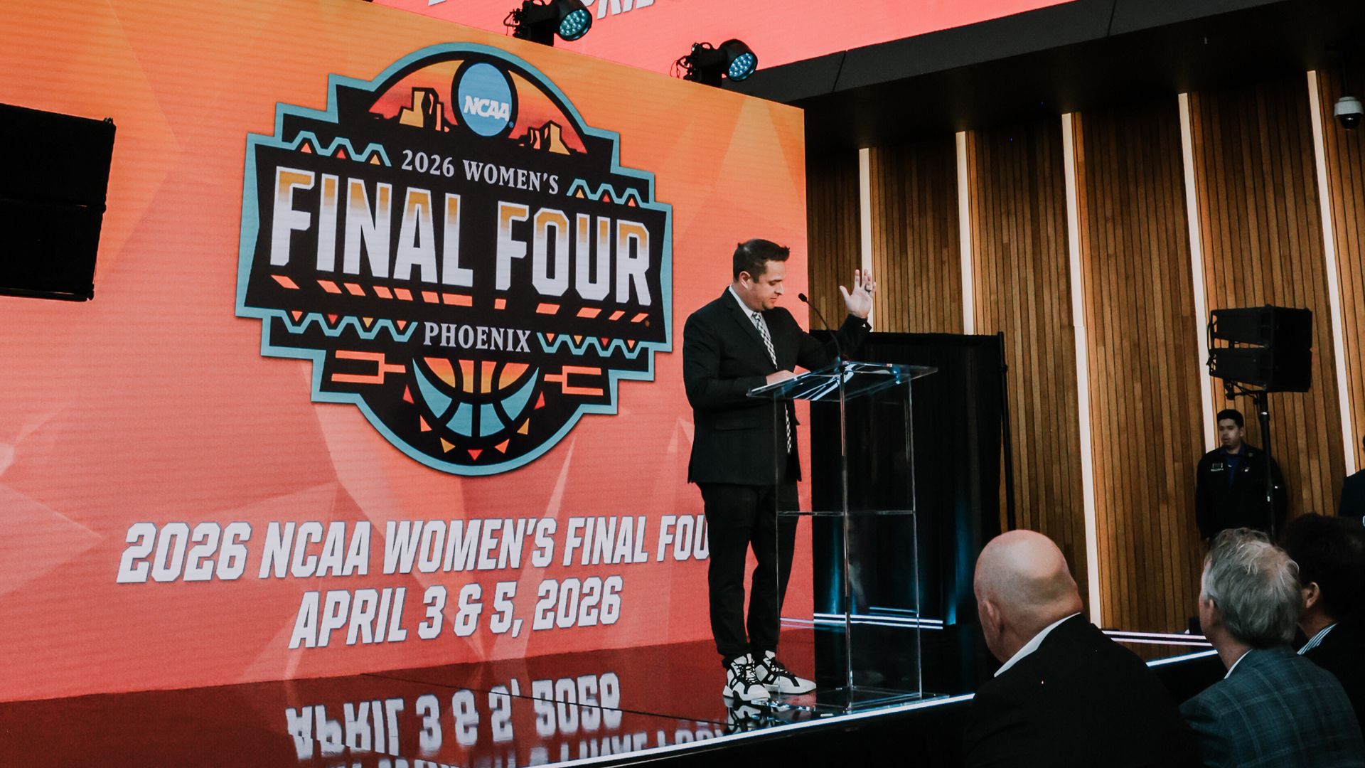 A man speaks at a podium in front of a large screen bearing the logo for the 2026 NCAA Women's Final Four.