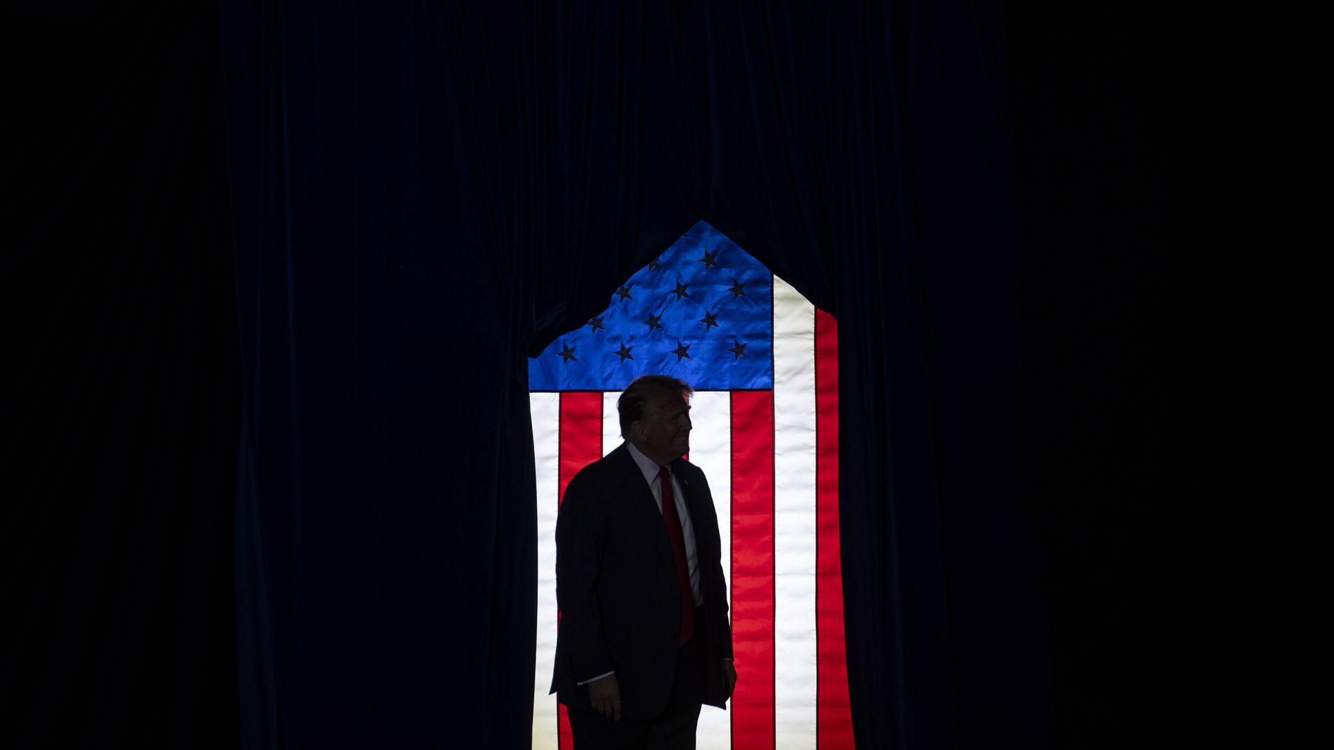 Former President Trump is shown in silhouette in front of a U.S. flag.