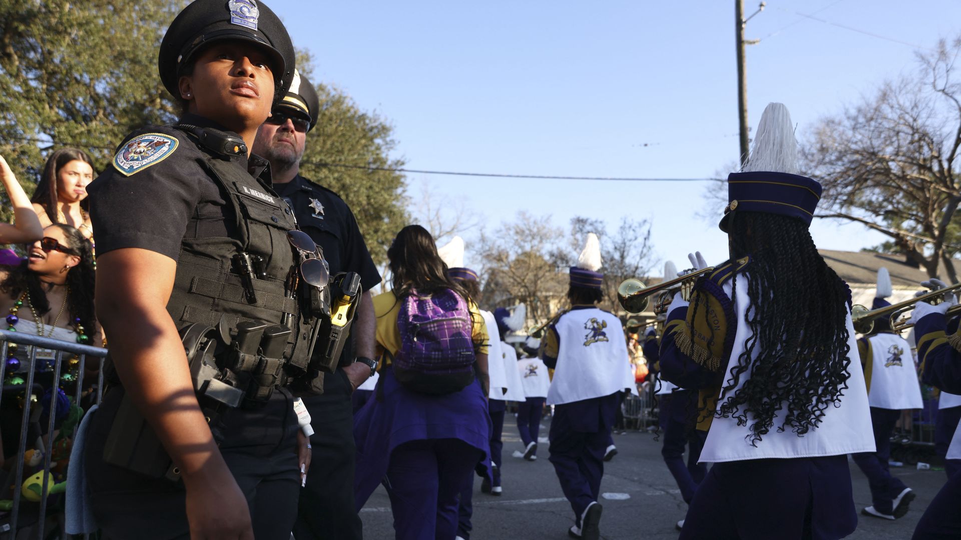Image shows a police officer in uniform with a marching band walking past.