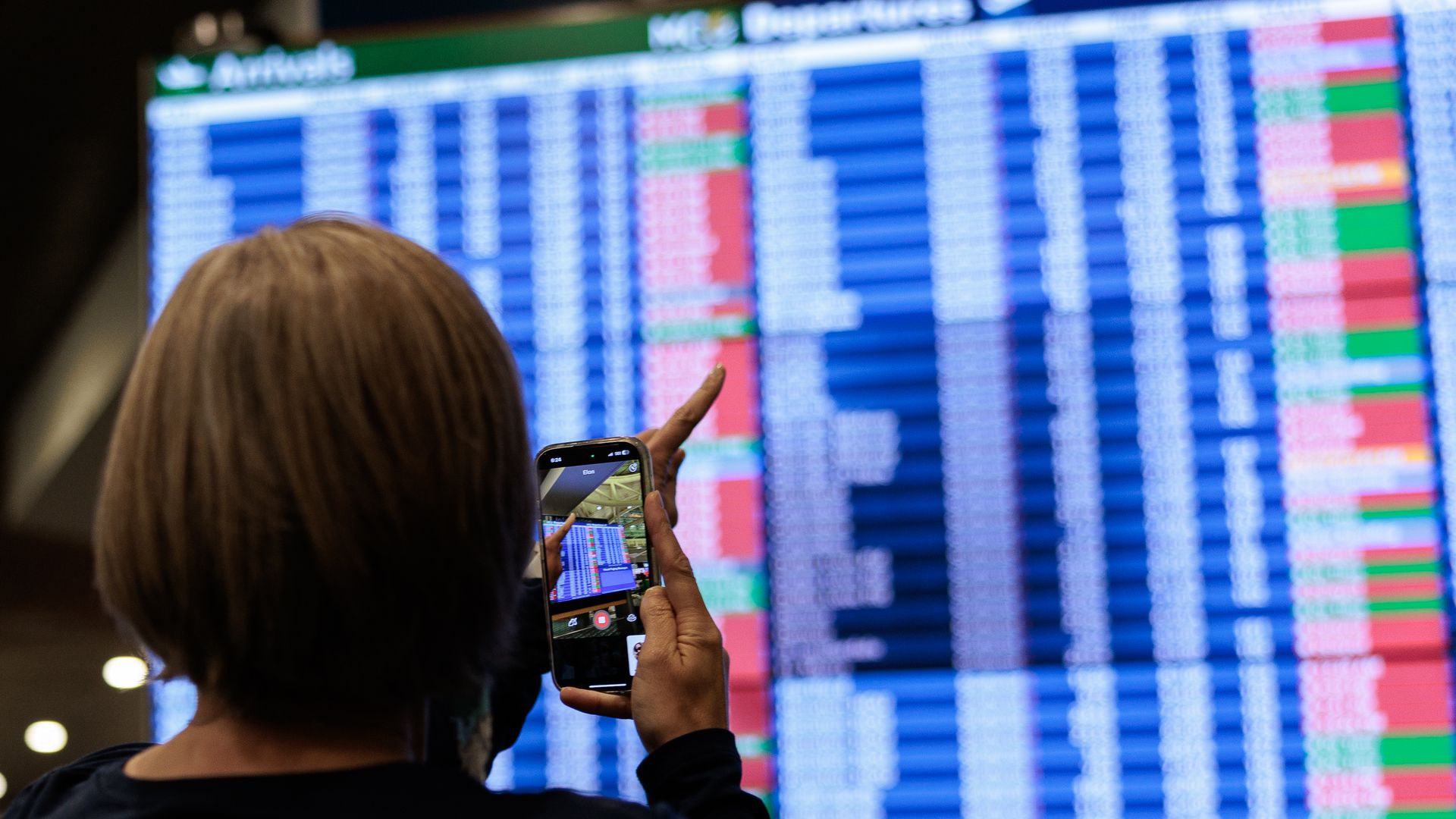A person photographed from behind taking a video of the departures screen  