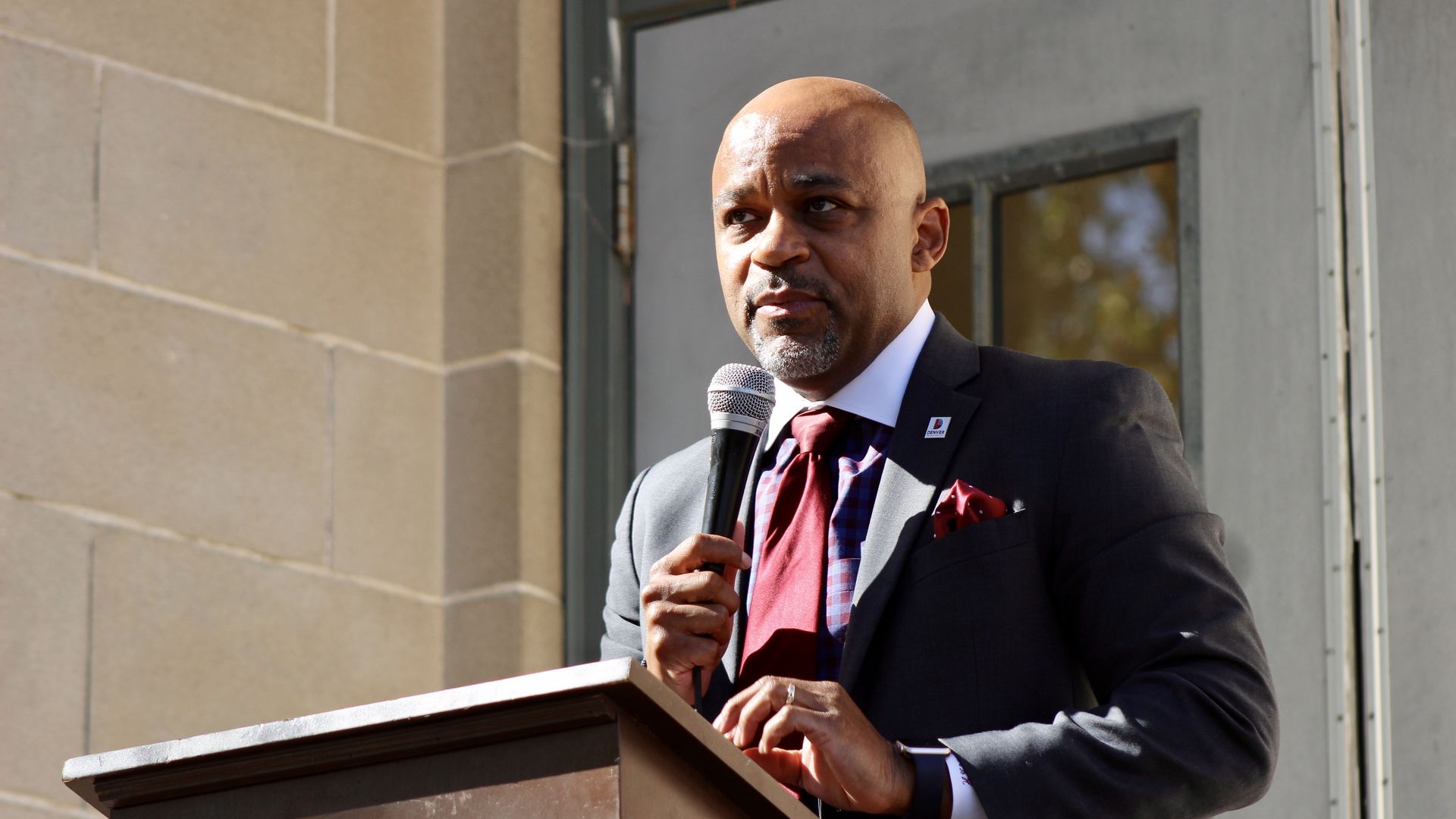 A photo of Mayor Michael Hancock outside standing behind a podium and holding a microphone 