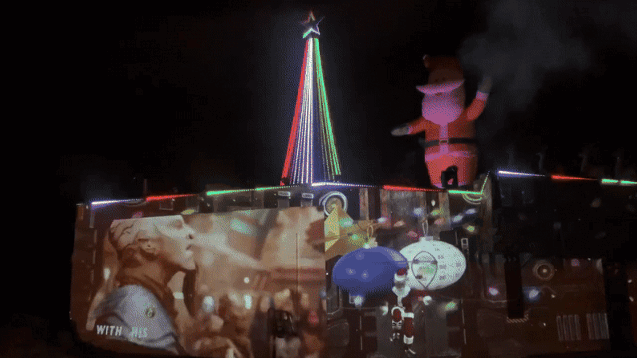 A GIF of fire shooting off the roof near an inflatable Santa and light-up Christmas tree.