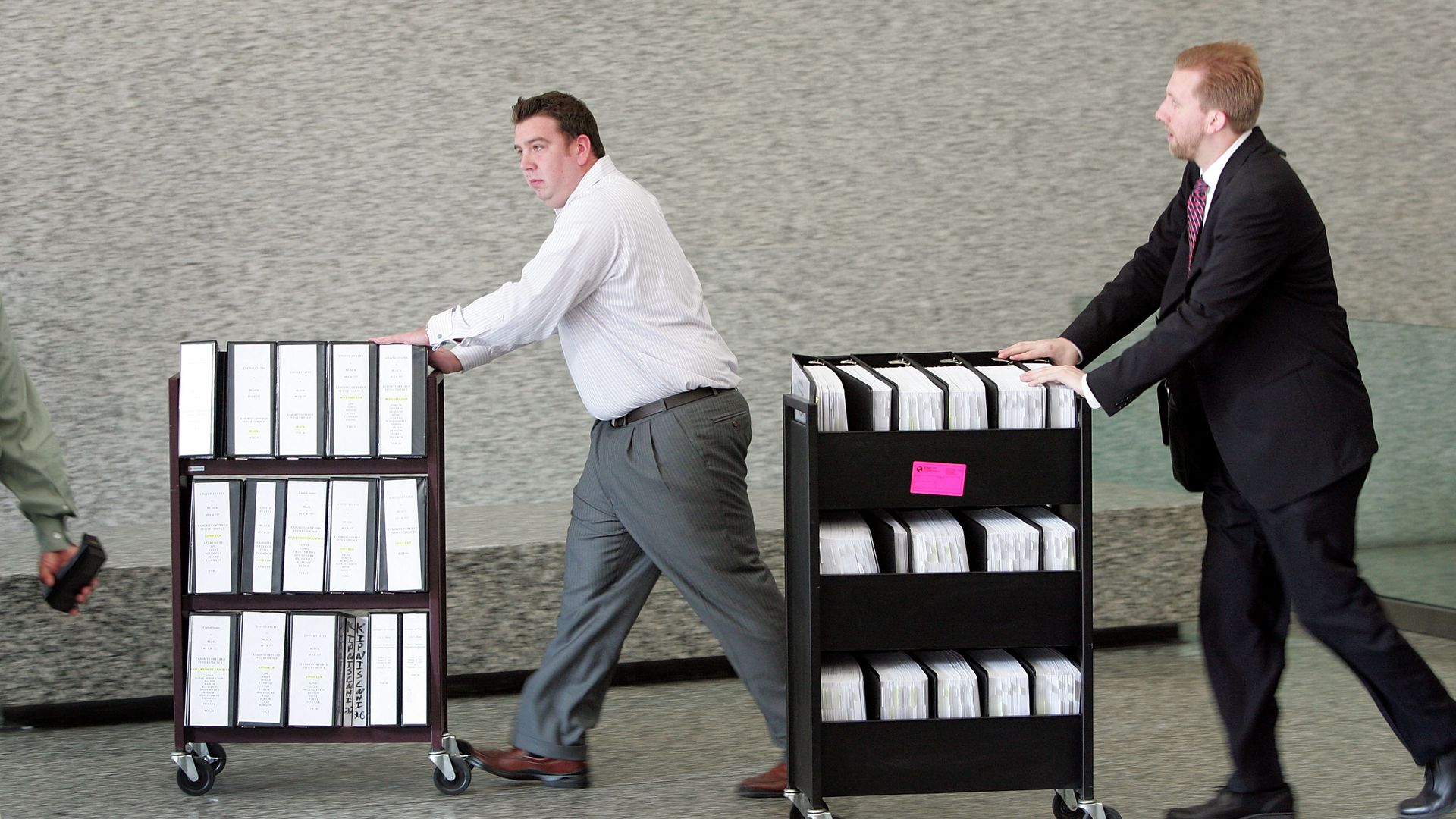 Two men wheeling carts full of white paper