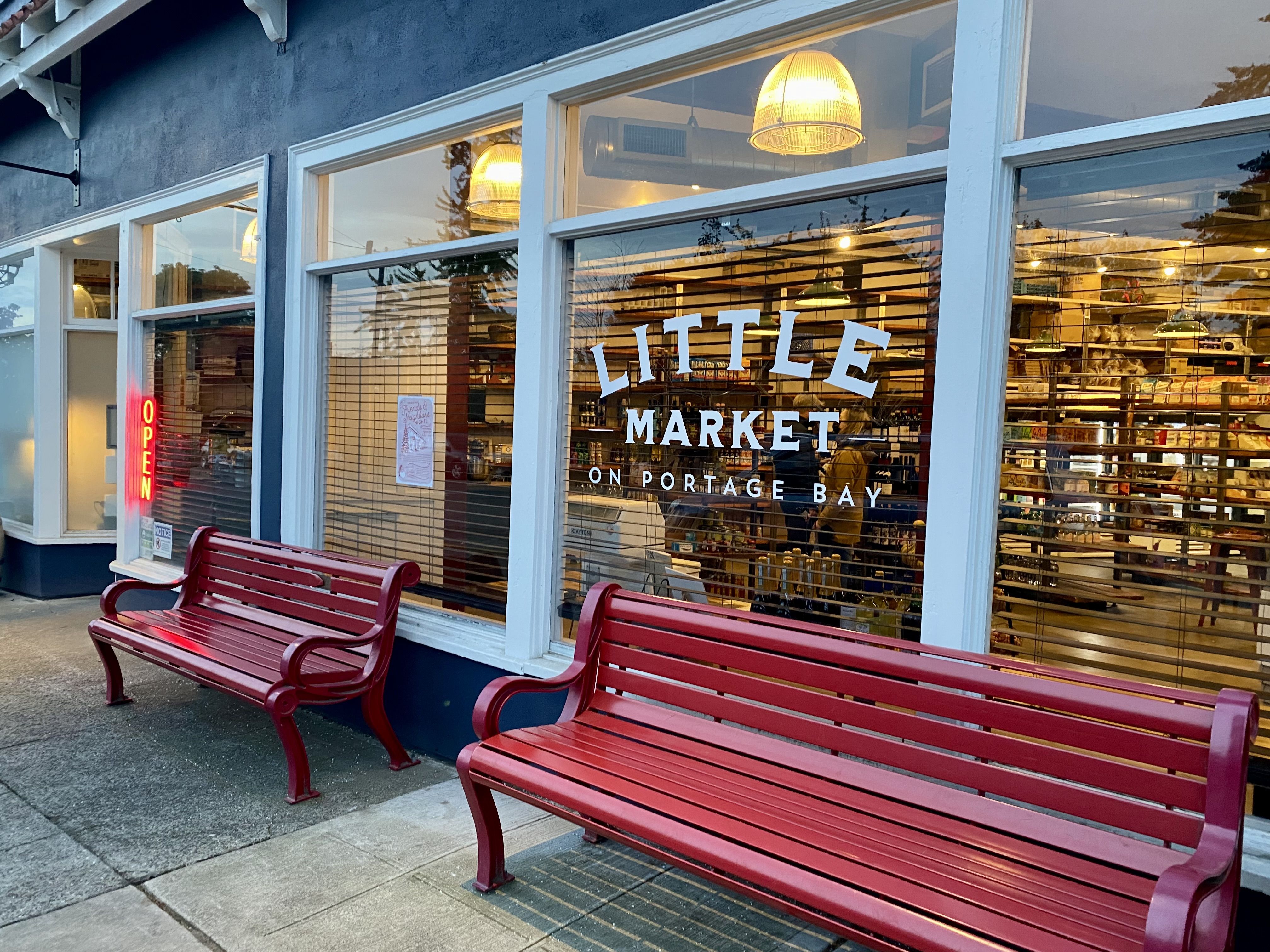 Red benches along a sidewalk, in front of a store window that says "Little Market on Portage Bay"