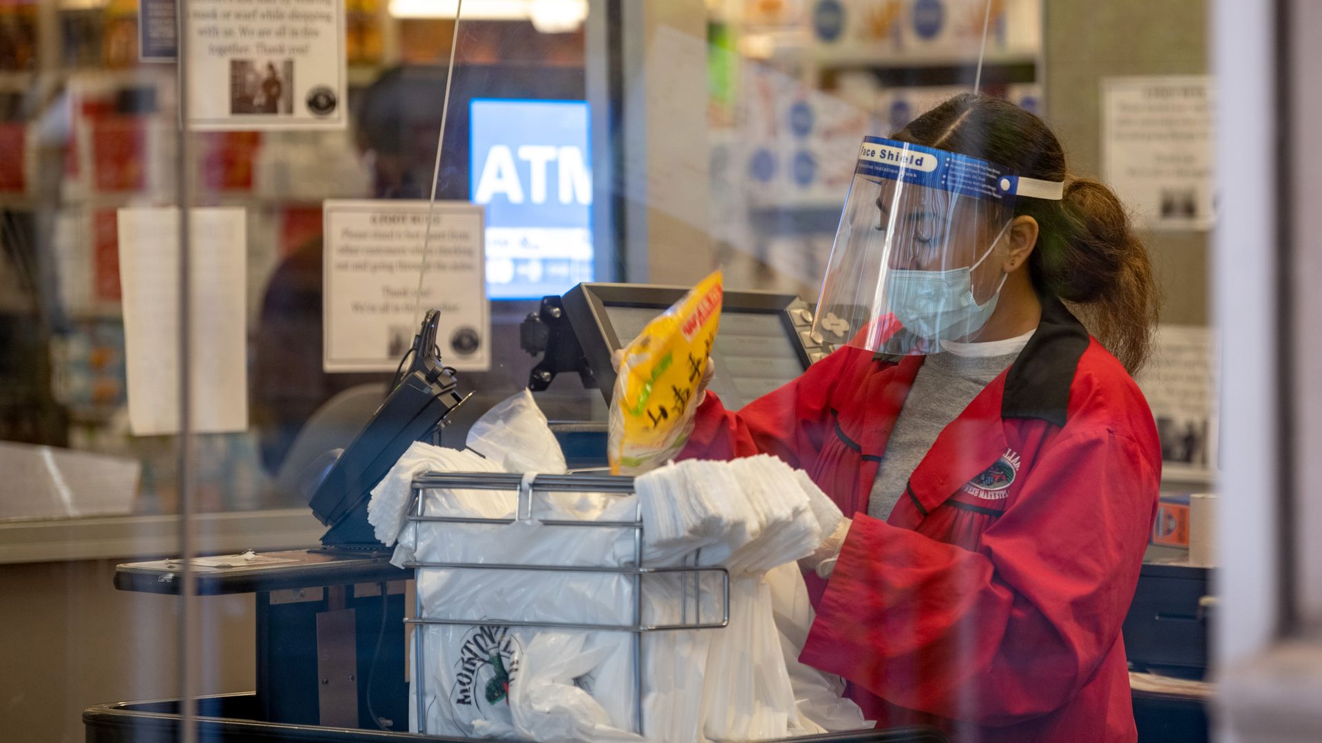 A grocery store worker bags items while wearing gloves, a face mask and a face shield