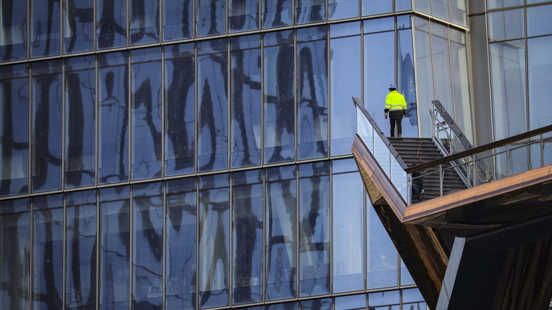 A construction worker stands at the end of a ladder in front of a New York skyscraper.