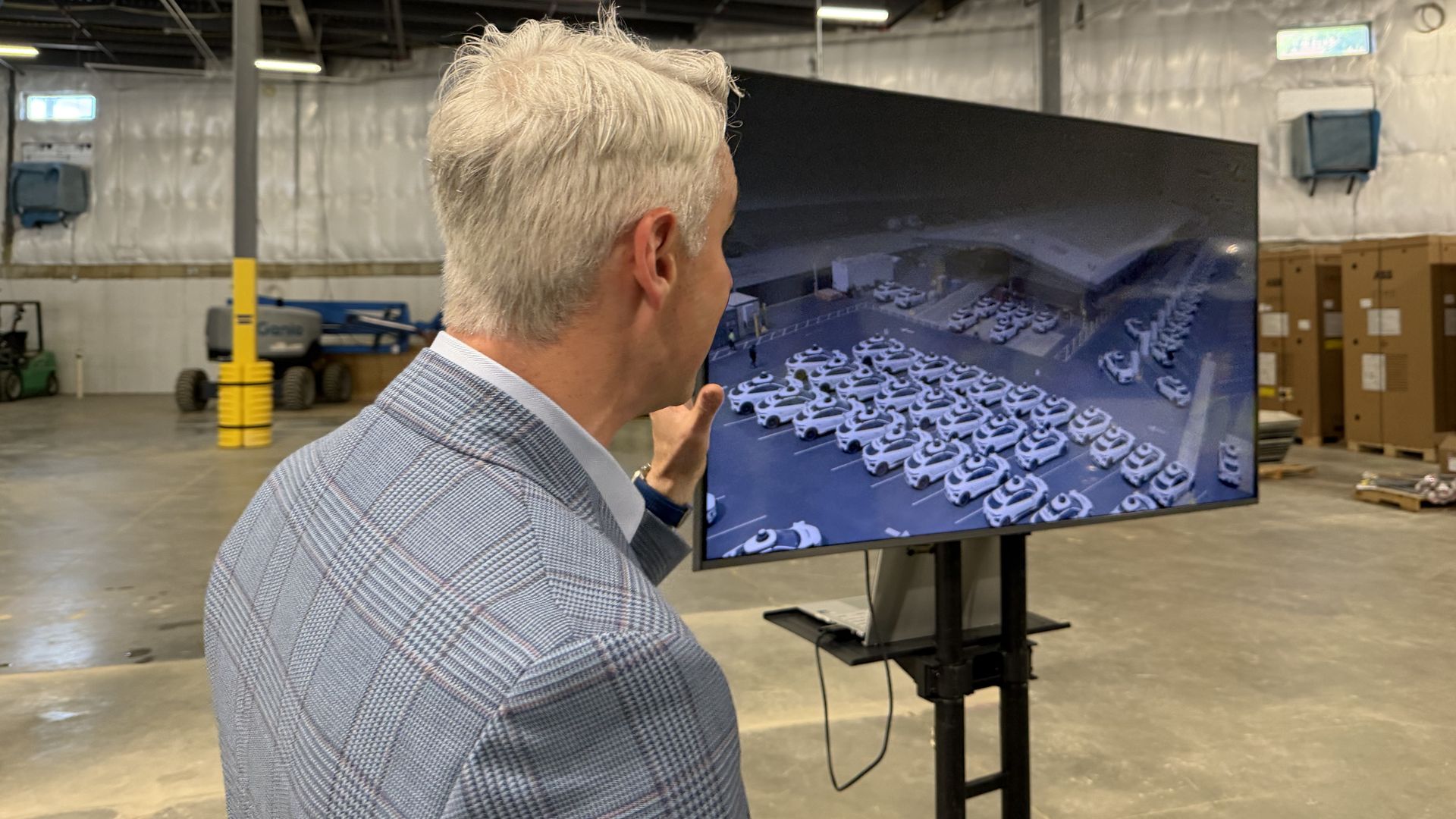 Waymo's Matt Walsh faces a TV screen that shows a company depot full of parked vehicles in San Francisco, inside a warehouse where the company is building a D.C. service facility.