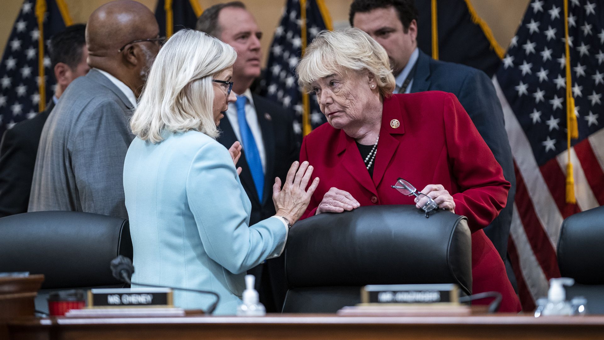 Rep. Liz Cheney, wearing a teal suit, speaks to Rep. Zoe Lofgren, wearing a red suit jacket and black shirt, at a Jan. 6 committee hearing. Behind them are Reps. Bennie Thompson and Adam Schiff.